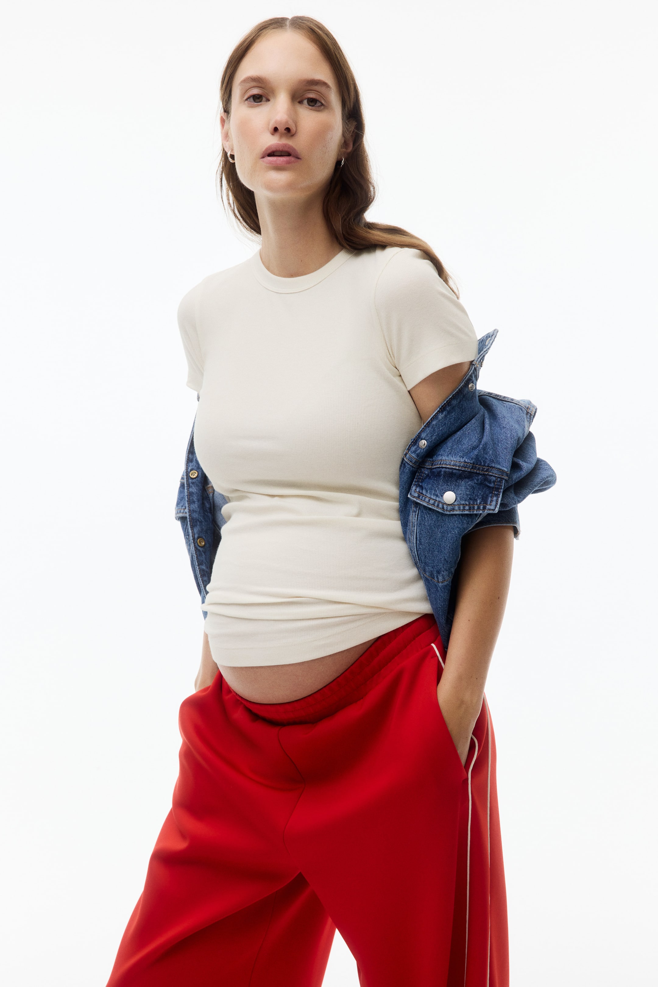 View larger image: A cream-coloured, ribbed knit, short-sleeved t-shirt fits closely on a body facing forward, accommodating a visible baby bump. It features a crew neck, and its hem rests above the waistline, revealing the lower part of the bump.