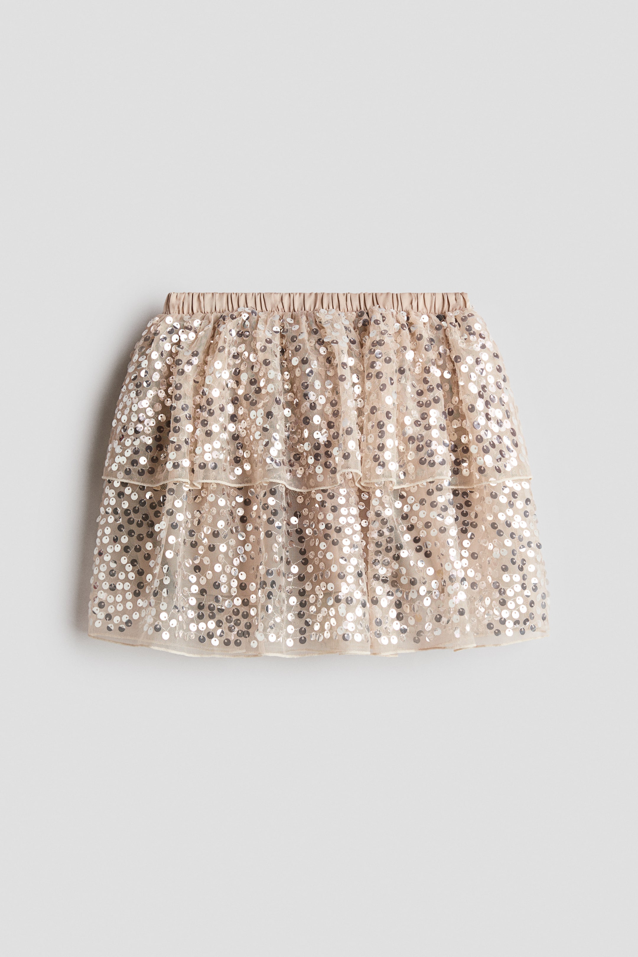 View larger image: A light beige, tiered skirt is shown from the front, featuring an elasticized satin waistband and two ruffled layers of sheer tulle adorned all over with silver sequins.