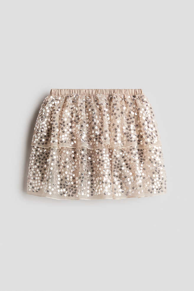 A light beige, tiered skirt is shown from the front, showcasing an elasticated satin waistband and two ruffled layers of sheer tulle embellished all over with silver sequins. - 1