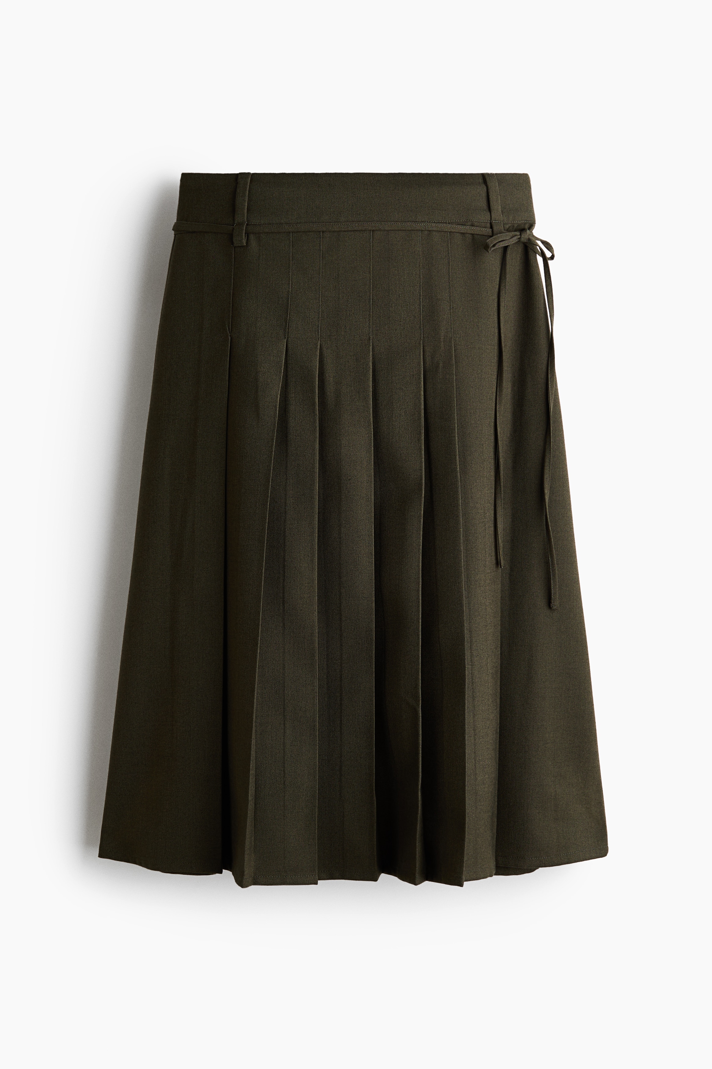 The model is wearing a calf-length A-line skirt in dark olive green twill with front pleats. The skirt is styled with a matching olive blazer, a draped olive green top, and tall black leather boots.