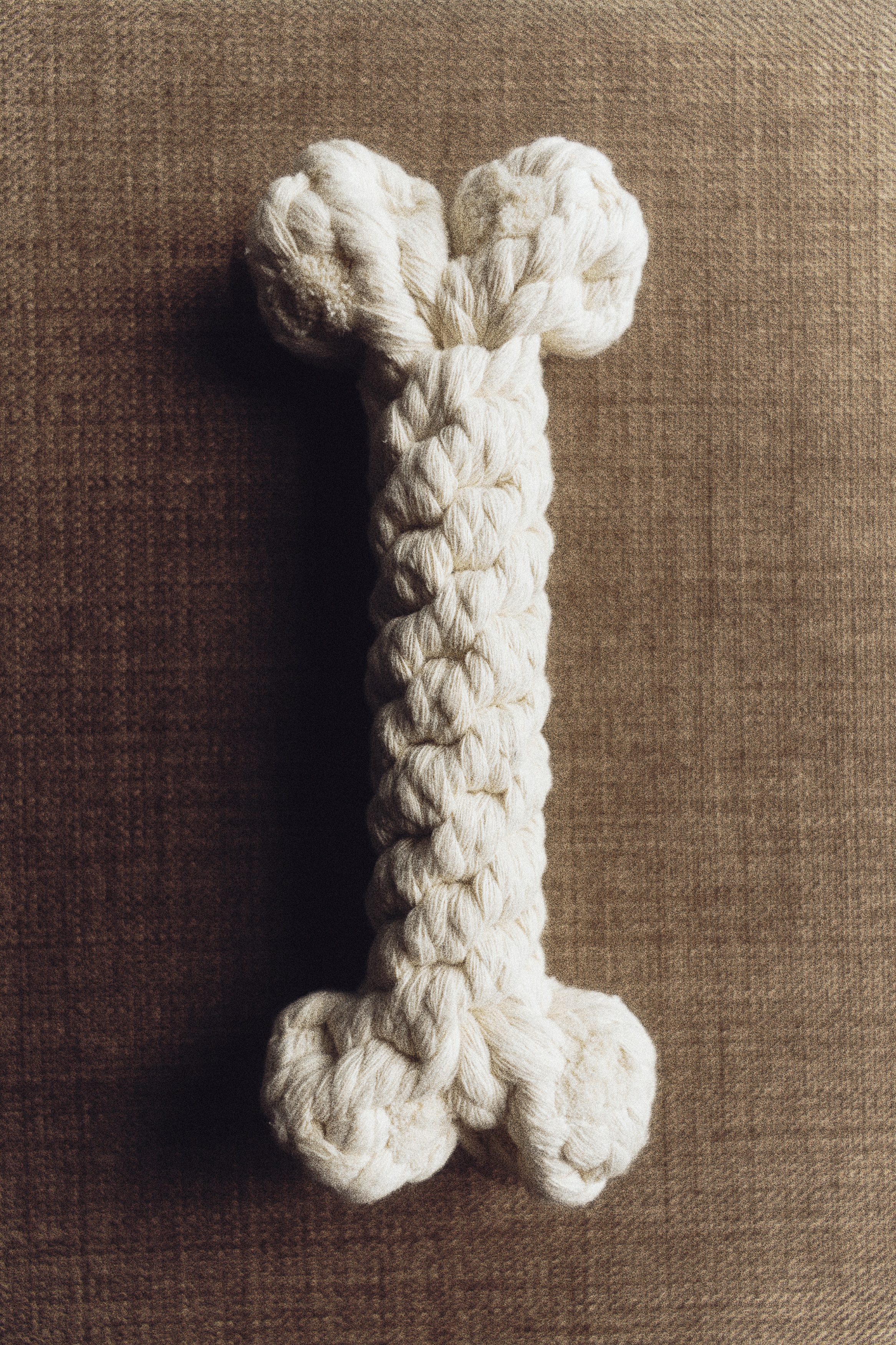 A bone-shaped dog toy made of off-white cotton rope is lying horizontally, facing front. The toy is displaying a thick, twisted central bar with large knotted ends that mimic bone joints.