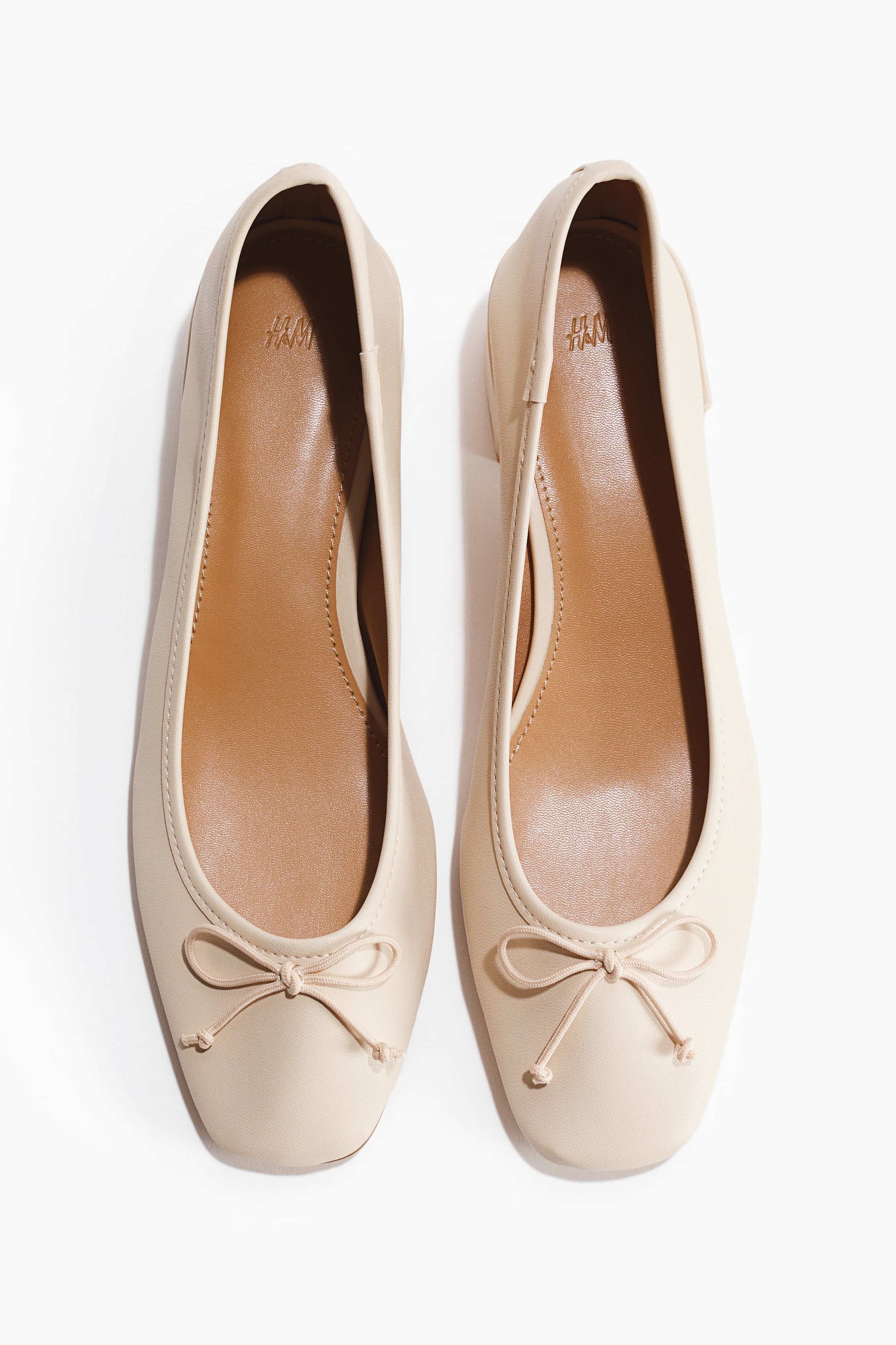 Grotere afbeelding bekijken: Een paar licht beige ballerina's met een vierkante neus, een kleine strik op de voorkant van elke schoen en een beige binnenzool met een H&M-logo.