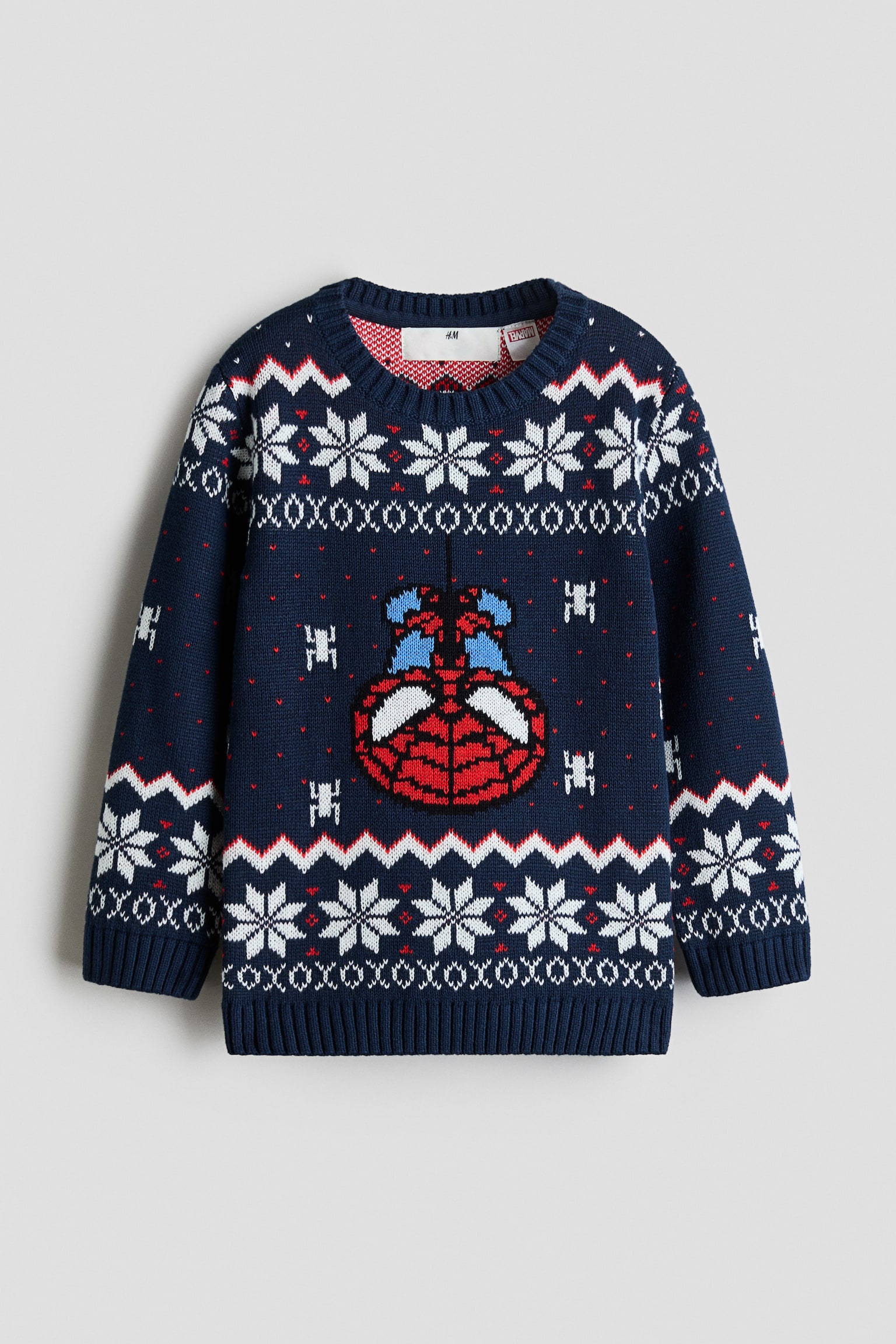 Un pull en maille bleu marine est prÃ©sentÃ© de face, avec un motif festif Fair Isle composÃ© de flocons de neige blancs, de rayures en zigzag rouges et blanches, ainsi quâun motif central reprÃ©sentant un masque Spider-Man Ã  lâenvers. Ce pull Ã  manches longues est dotÃ© dâun col rond cÃ´telÃ©, de poignets cÃ´telÃ©s et dâun ourlet cÃ´telÃ©.