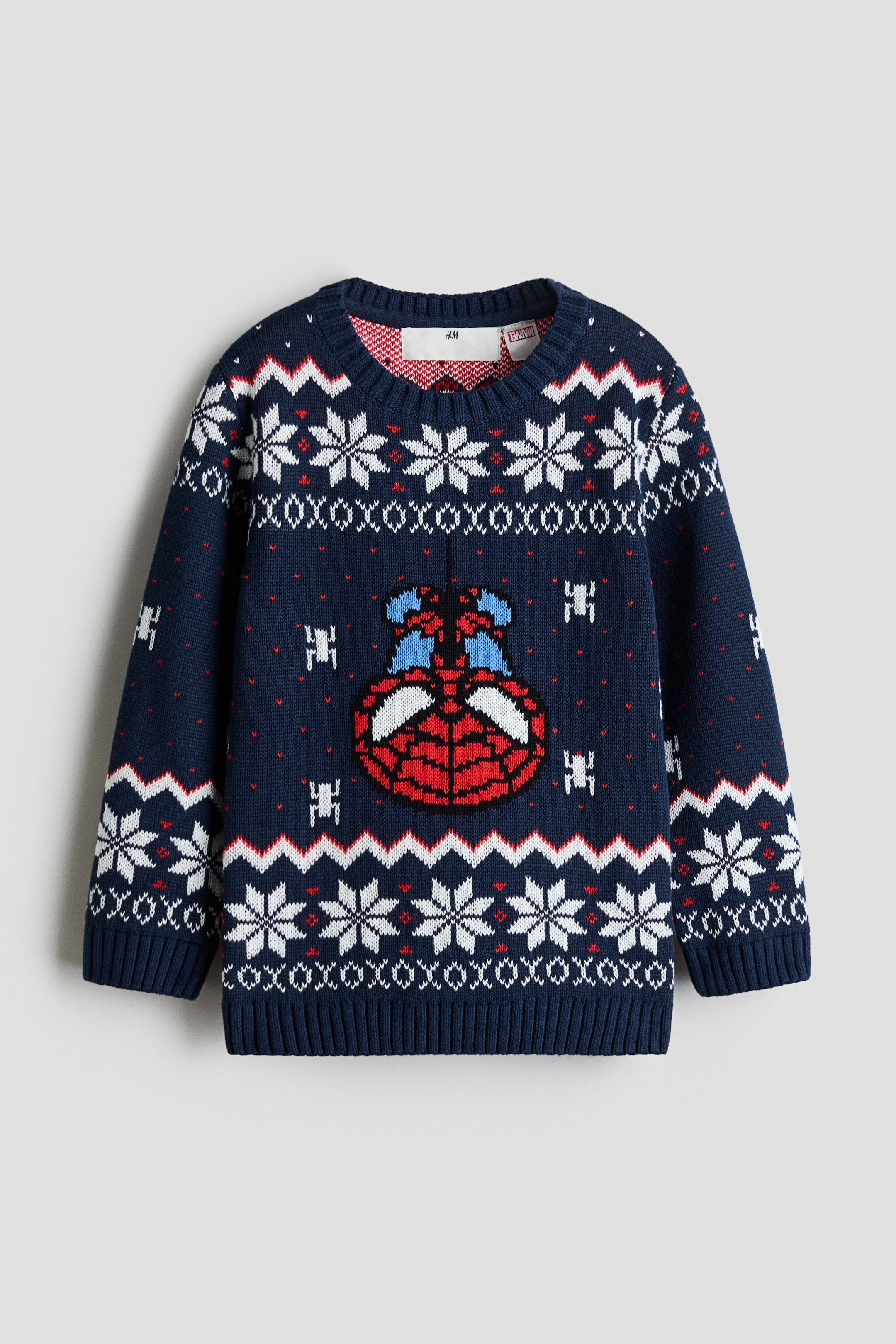 View larger image: A navy blue knit sweater is shown from the front, featuring a festive Fair Isle pattern with white snowflakes, red and white zigzag stripes, and a central graphic of an upside-down Spider-Man mask. The long-sleeved sweater is designed with a ribbed crew neck, ribbed cuffs, and a ribbed hem.