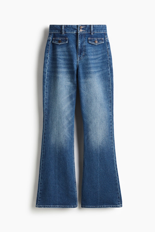 Blauwe denim jeans worden weergegeven als VOORZIJDE, met een hoge taille, een ritssluiting en twee knopen. Ze zijn ontworpen met een slanke pasvorm door de dij, uitlopend vanaf de knie, en hebben twee decoratieve klepzakken met knopen aan de voorkant, met een lange lengte die op de zoom valt. - 1