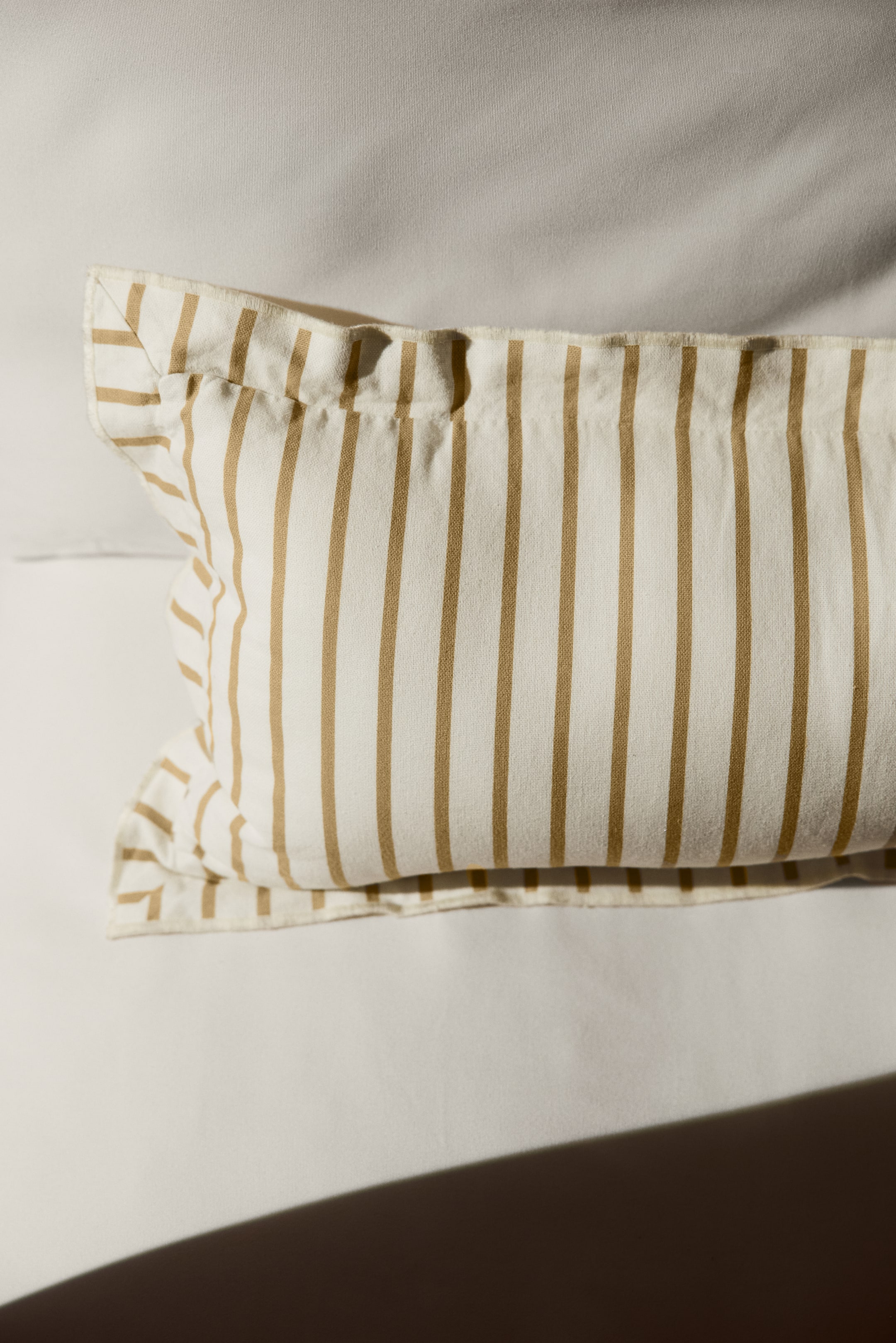 View larger image: A rectangular pillow showcases vertical tan stripes on an off-white fabric. Positioned horizontally, it is angled slightly upwards and to the left, featuring a folded flap along its top edge.