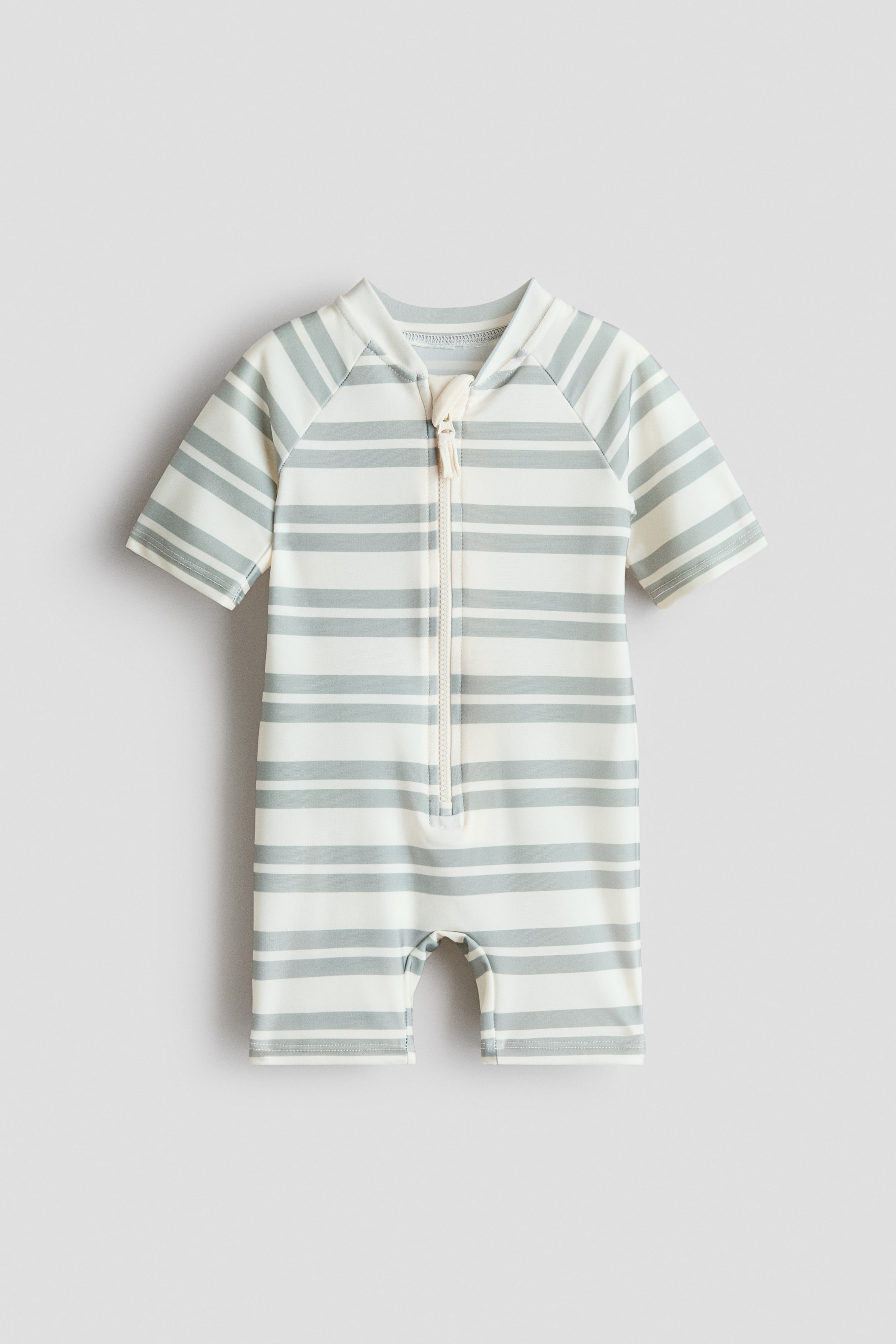 Ver imagen más grande: Un traje de baño presenta su FRONTAL, con una base blanca y rayas horizontales en gris claro. Está diseñado con un cuello alto, mangas raglán cortas y una cremallera frontal blanca que se extiende hasta la mitad del torso, terminando con piernas cortas.