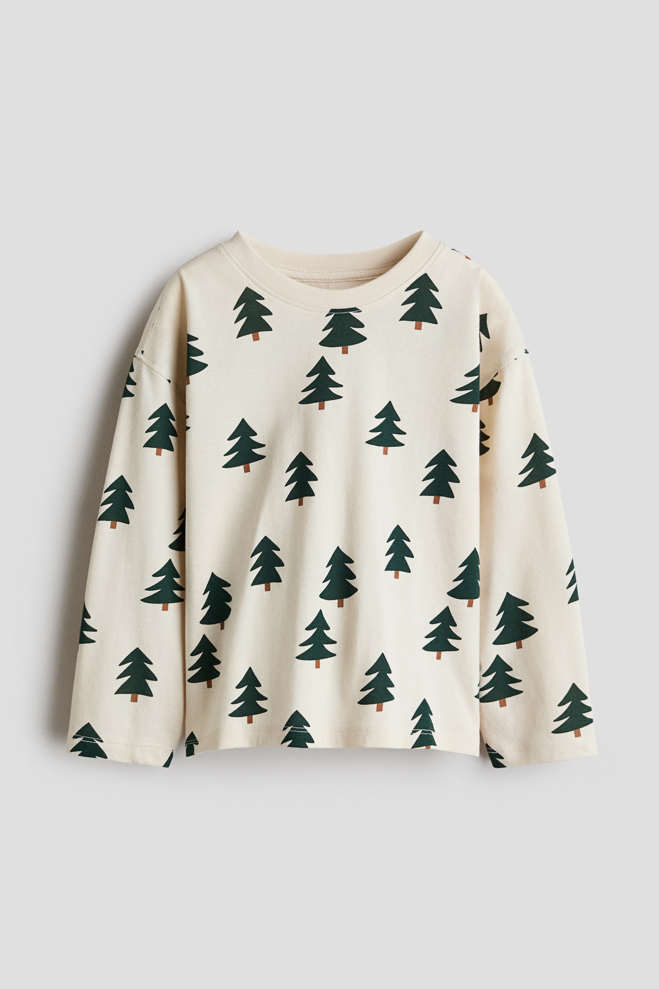 View larger image: A cream-coloured, long-sleeve tee is shown from the front, featuring an all-over print of green pine trees with brown trunks. The garment is designed with a round neckline with a ribbed trim and dropped shoulders.
