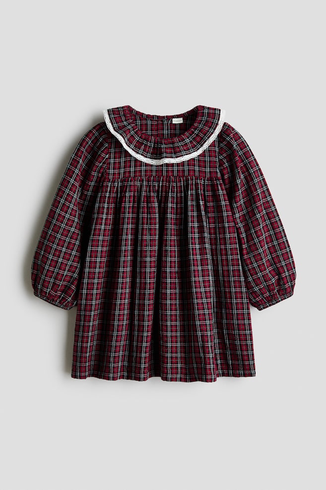 O rochie din bumbac Ã®n linie A este prezentatÄ din faÈÄ, avÃ¢nd un model Ã®n carouri roÈu, negru Èi alb. Rochia este conceputÄ cu un guler rotund cu finisaj din dantelÄ albÄ, un platou Ã®ncreÈit care creeazÄ o siluetÄ evazatÄ Èi mÃ¢neci lungi, voluminoase, cu manÈete elastice. - 1