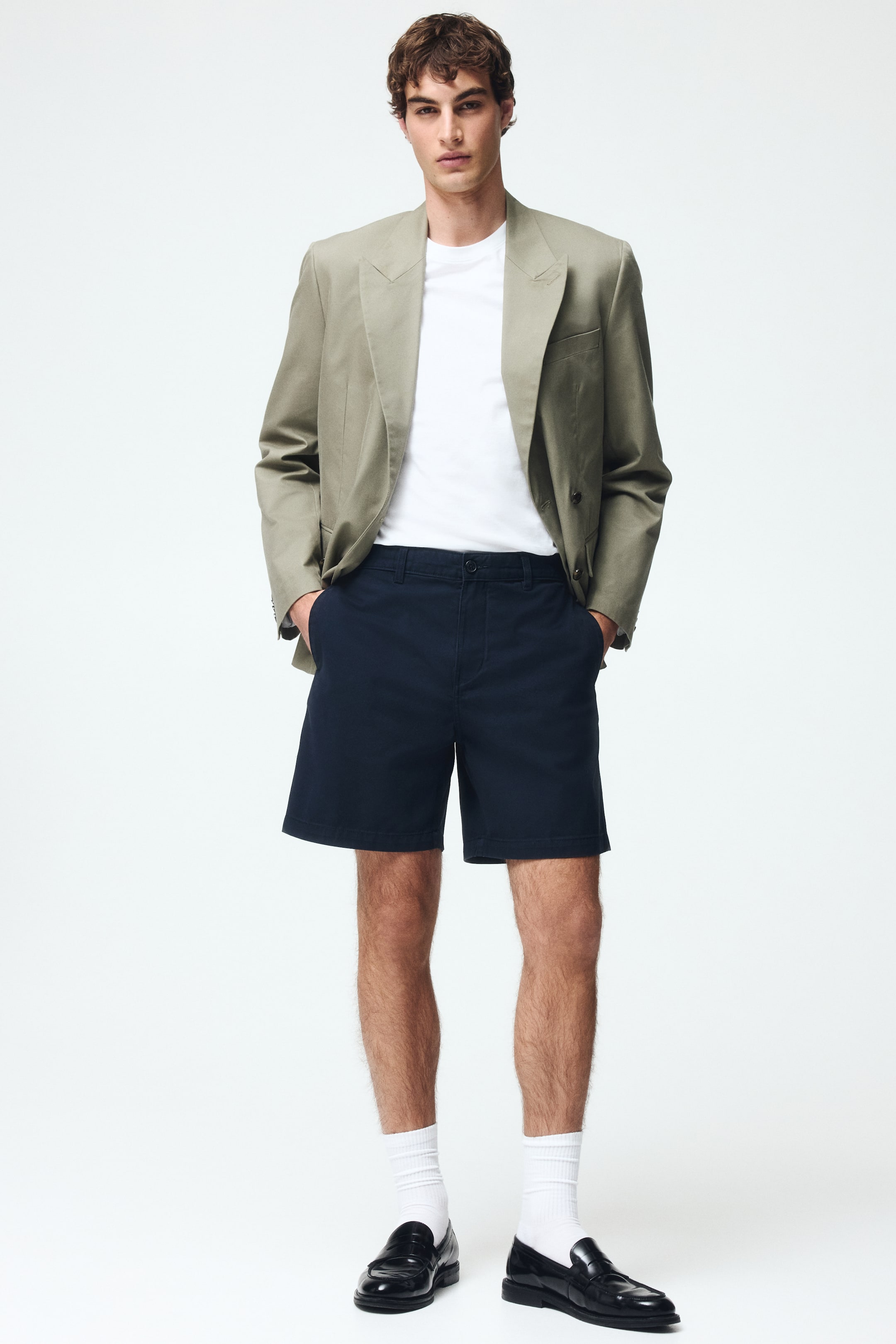 View larger image: Navy blue shorts are showcased from a front-facing angle, featuring a relaxed fit that extends just above the knee. They display a flat front with a button closure, zipper fly, and side pockets.