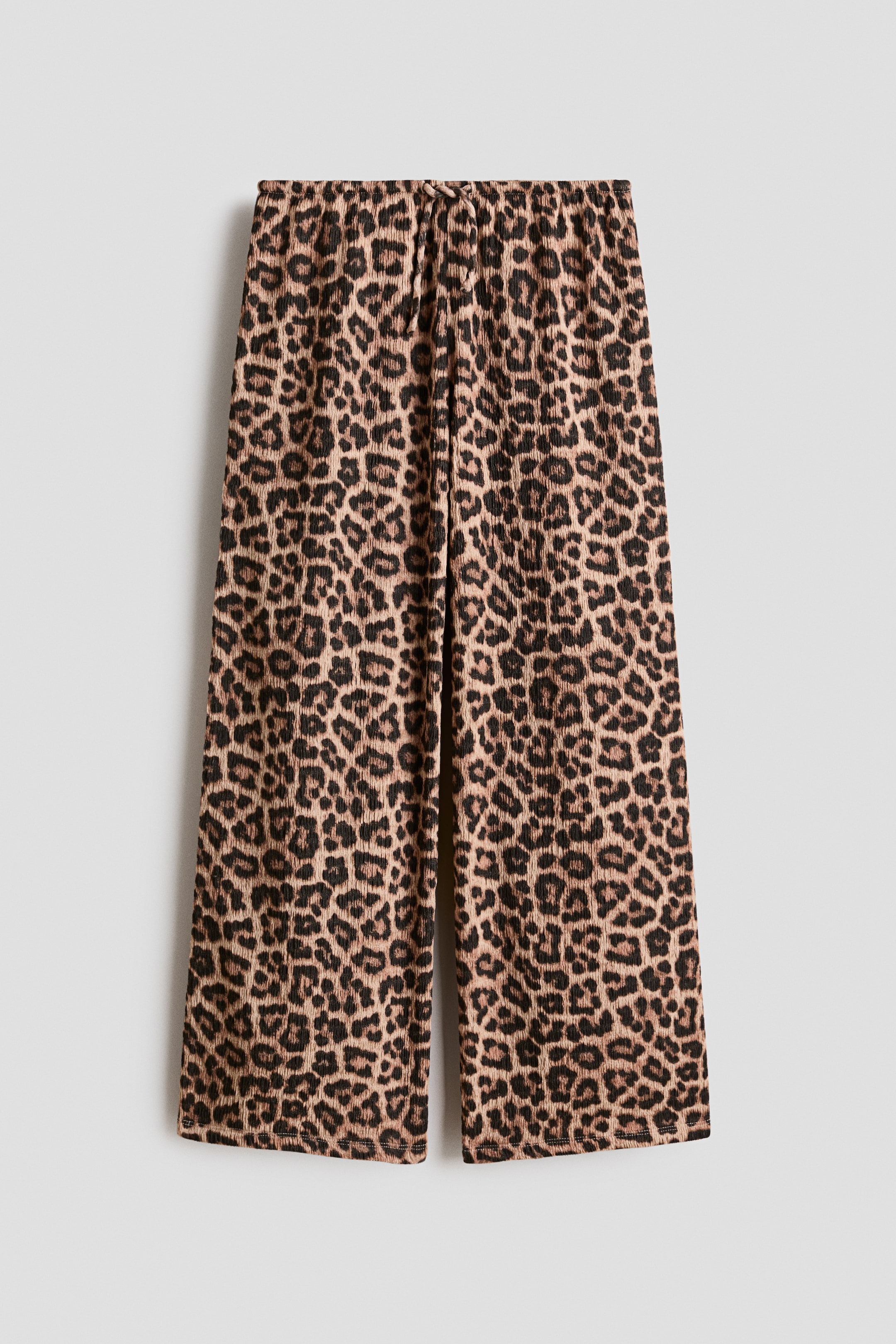 Se større billede: Bukserne viser et leopardprint på et blødt, struktureret jersey-stof, præsenteret fra forsiden. De har en elastisk talje med snøre og lige ben.