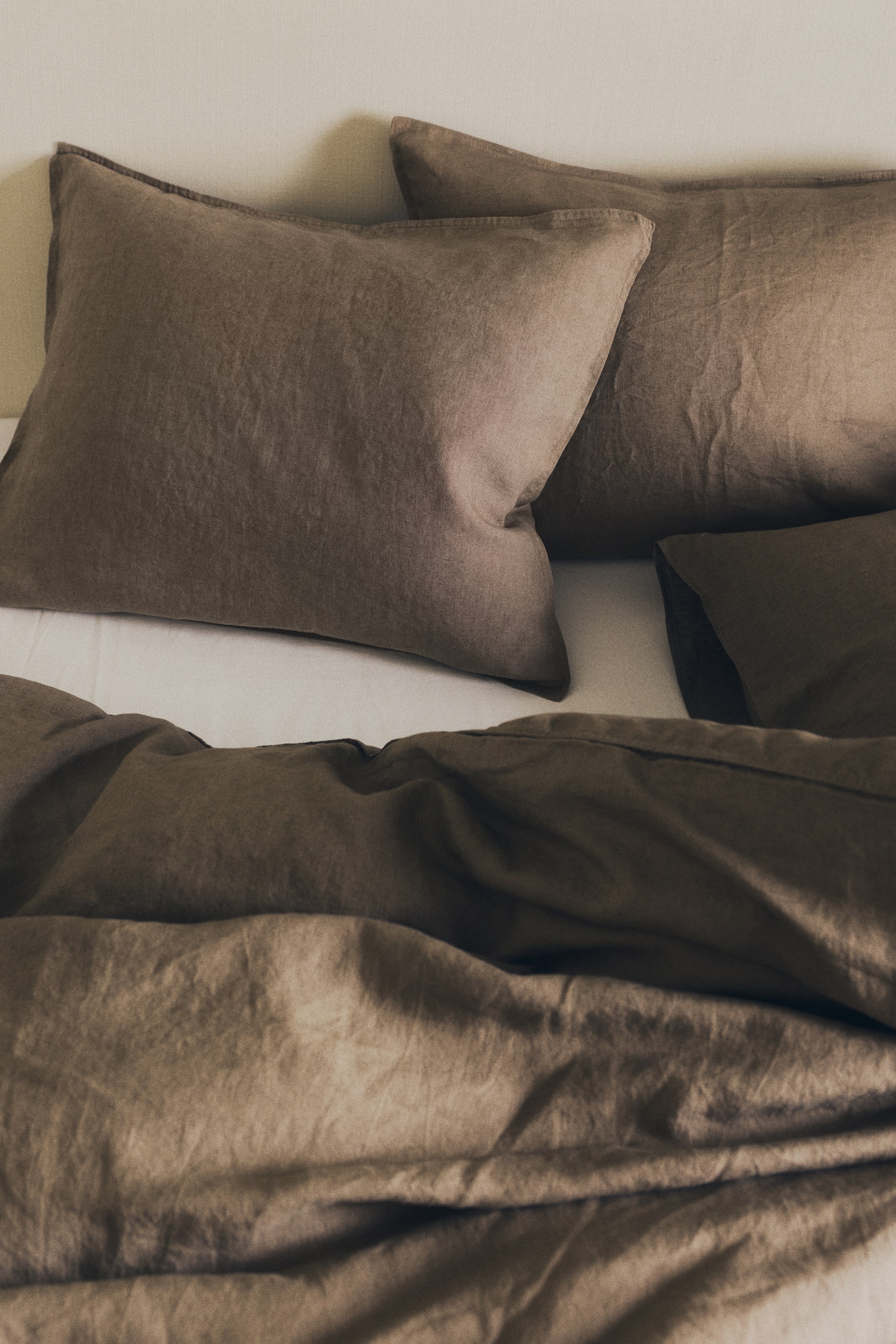 View larger image: Washed linen pillowcases in a dark taupe color are resting on a bed, showcasing their textured, crinkled fabric and double-stitched edges.