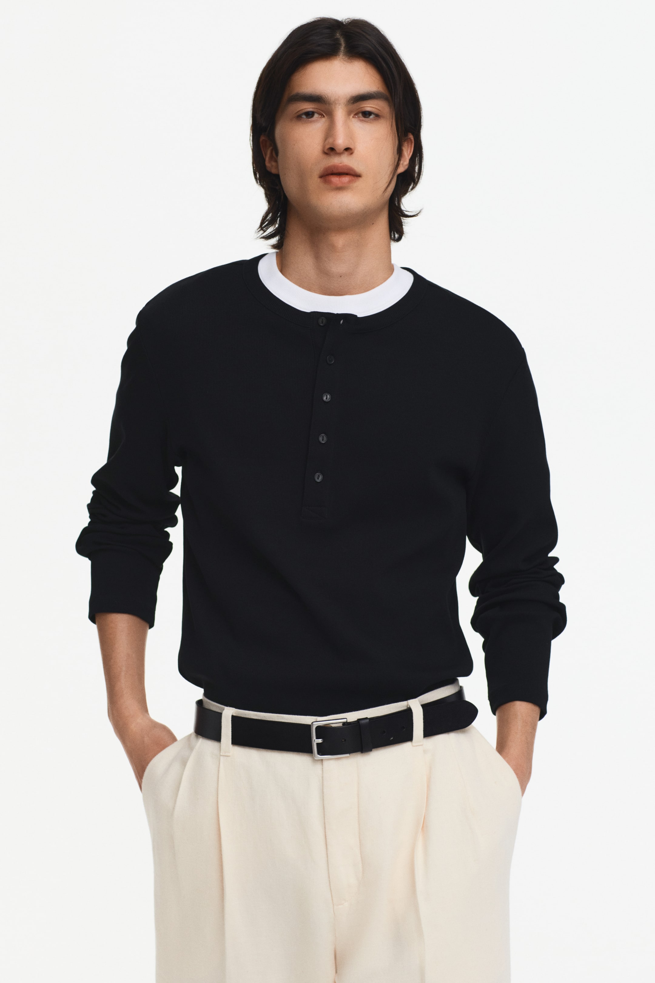 View larger image: The black long-sleeved Henley top showcases a ribbed texture and features a five-button placket. A white crew neck undershirt subtly peeks out from beneath the round neckline.