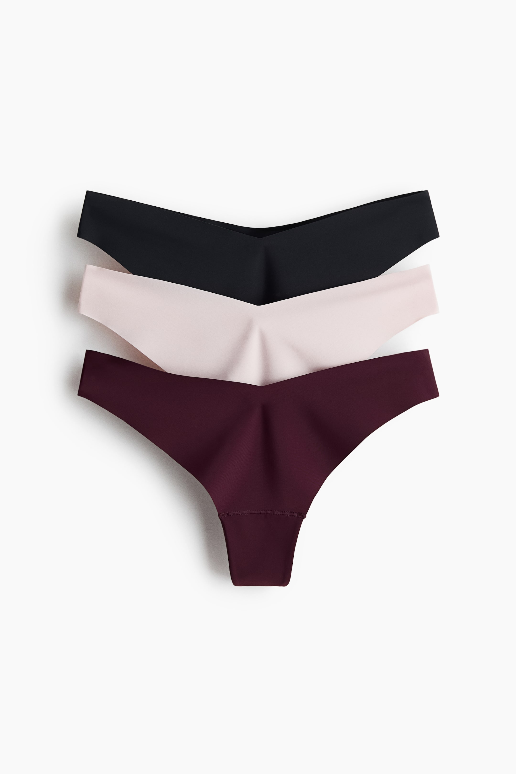 View larger image: Three microfibre thong briefs are stacked, showcasing their front. The top brief is black, the middle is light pink, and the bottom is burgundy, all featuring a low, V-shaped waist, a lined gusset, and laser-cut edges.