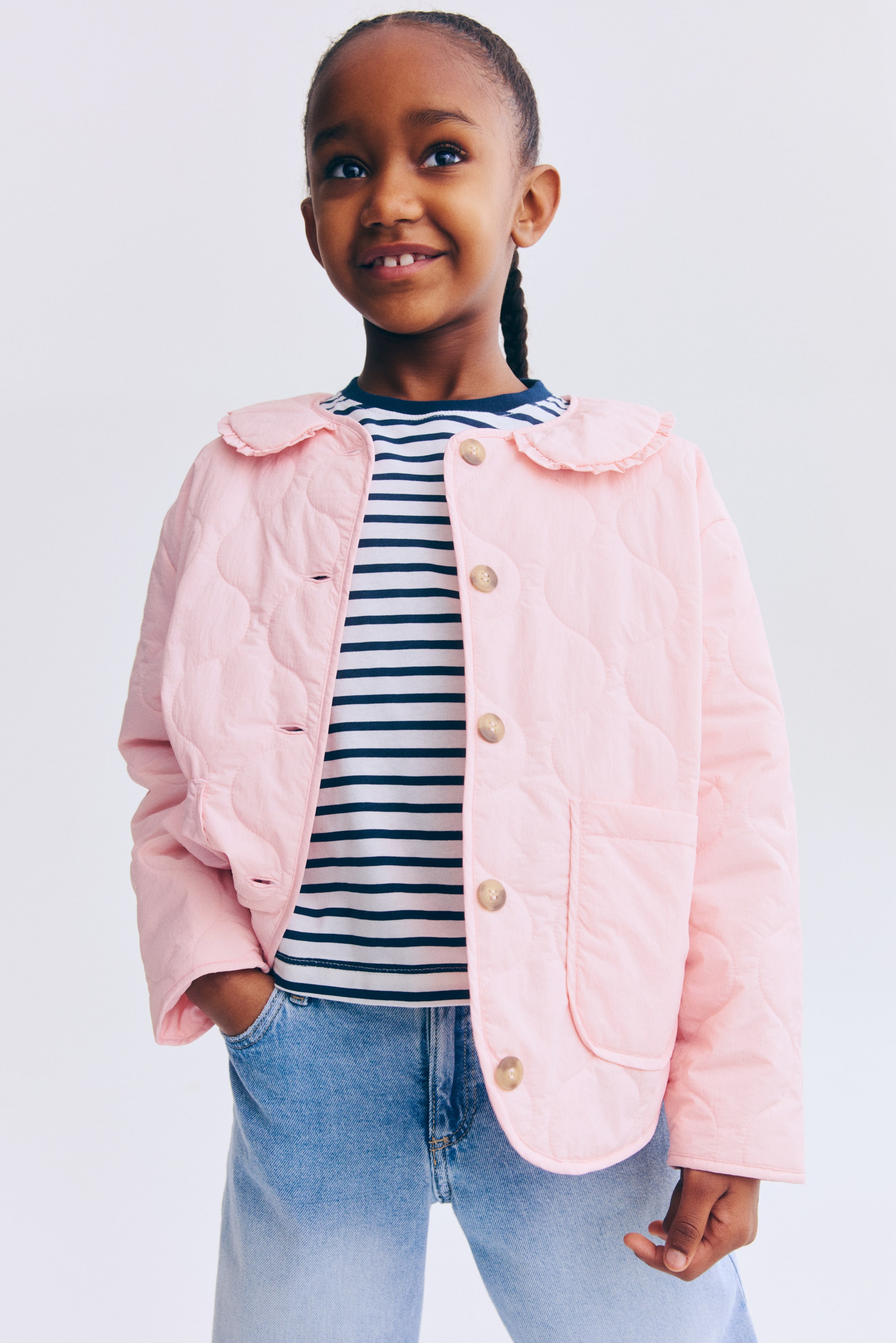 View larger image: A pink quilted jacket is worn open, revealing a striped shirt underneath. It features a ruffled collar, light-brown buttons and two front patch pockets, with the quilting forming a heart-like pattern.