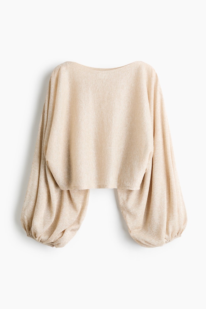 En kort, oversized stickad topp i skimrande ljusbeige fÃ¤rg hÃ¤nger vÃ¤nd framÃ¥t och har en bÃ¥tringning samt en kortad fÃ¥ll. Toppen visar lÃ¥nga, voluminÃ¶sa capÃ¤rmar med smala elastiska Ã¤rmslut som skapar en puffig, draperad siluett. - 1