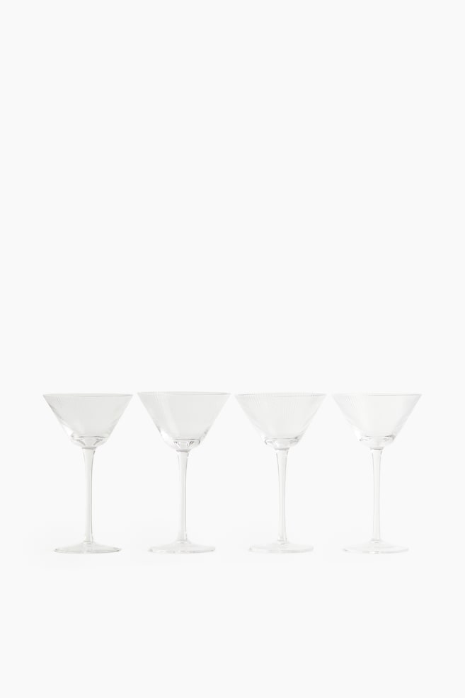Four clear cocktail glasses are standing in a row, all facing front. Each glass is designed with a fluted design on its conical bowl. - 1