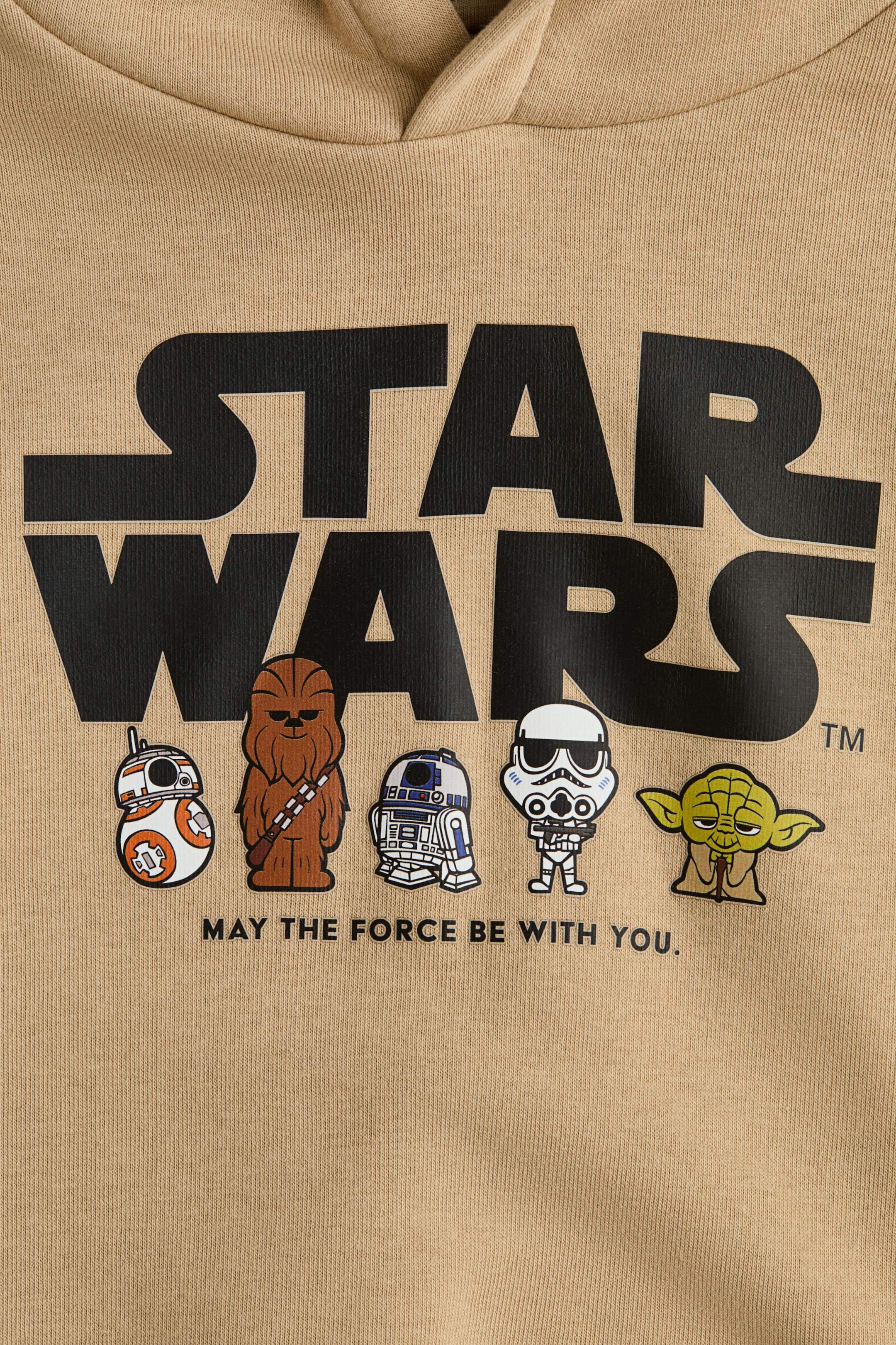 Προβολή μεγαλύτερης εικόνας: Ένα καφέ φούτερ με κουκούλα βρίσκεται επίπεδα, με την κουκούλα να είναι ορατή στην κορυφή. Το μπροστινό μέρος, κατασκευασμένο από ένα ορατό πλεκτό ύφασμα, εμφανίζει ένα μεγάλο μαύρο λογότυπο "STAR WARS", κάτω από το οποίο είναι ορατές καρτούν εικονογραφήσεις των BB-8, Chewbacca, R2-D2, ενός Stormtrooper και του Yoda, ακολουθούμενες από το κείμενο "MAY THE FORCE BE WITH YOU."