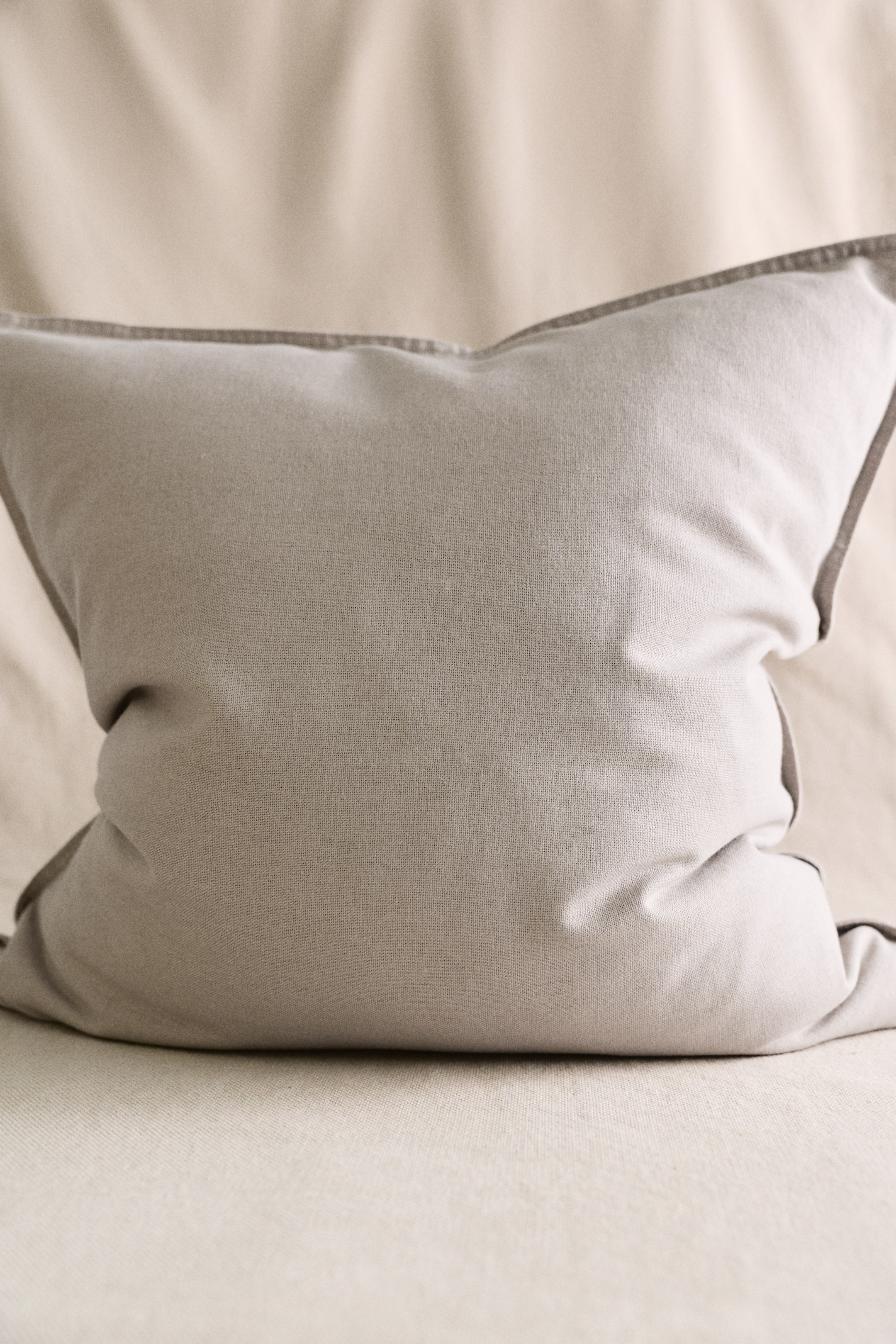 View larger image: A light grey rectangular cushion is positioned upright and facing forward, showcasing a dark grey piped trim along its edges and displaying subtle creases on its surface.