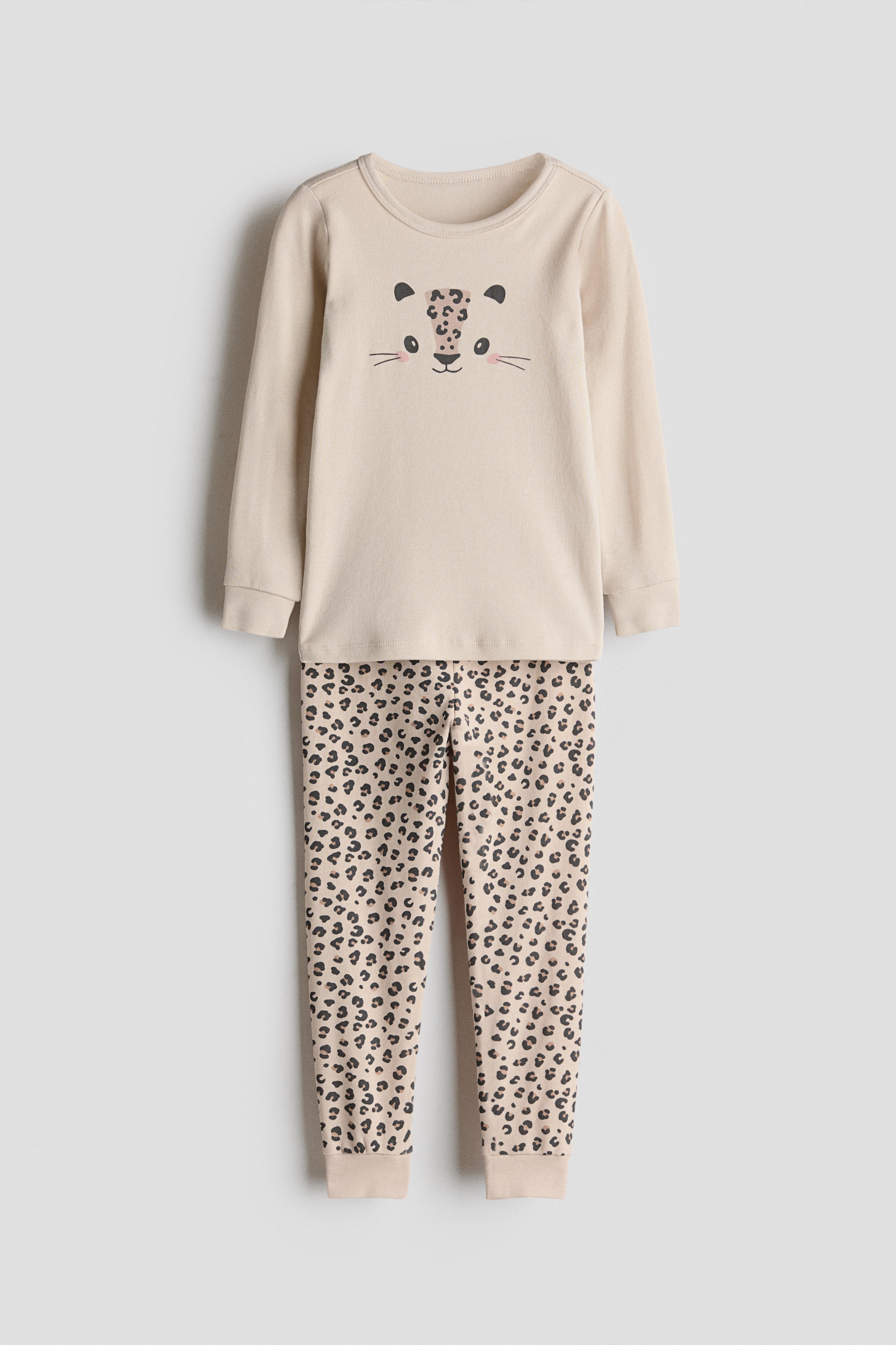 View larger image: Snug Fit printed cotton pyjamas feature a light beige, long-sleeved top with a round neck and ribbed cuffs, displaying a leopard face graphic print on the front. The matching trousers showcase an all-over black leopard spot print on a light beige background, ending in ribbed ankle cuffs.