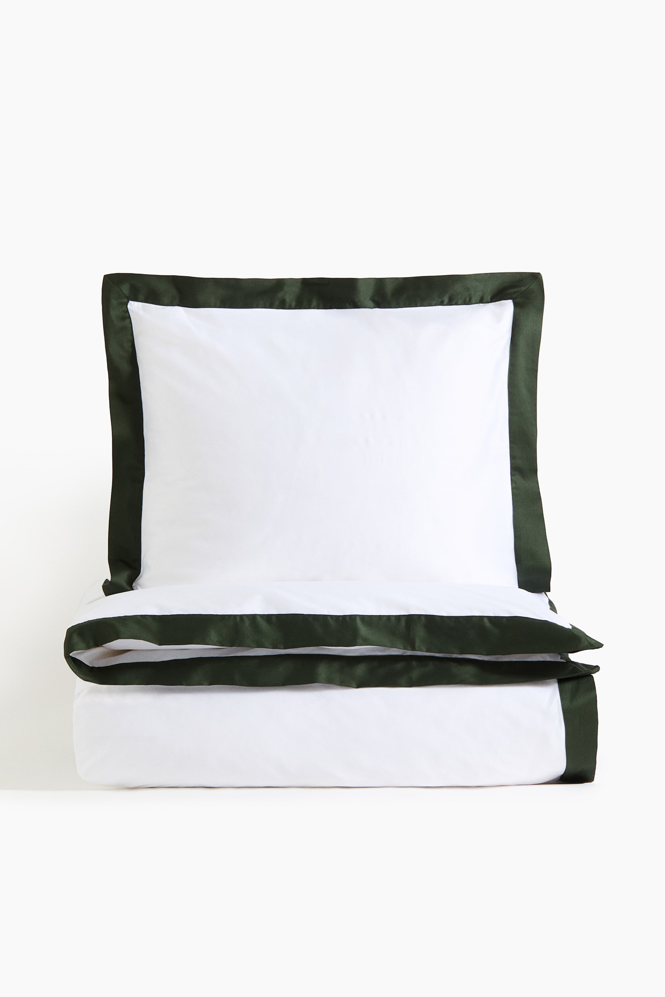 View larger image: A white pillow sham is showcasing a dark green satin-like border around its perimeter, resting on a folded white duvet cover. The duvet cover is also featuring a matching dark green border along its top edge, complementing the pillow sham.