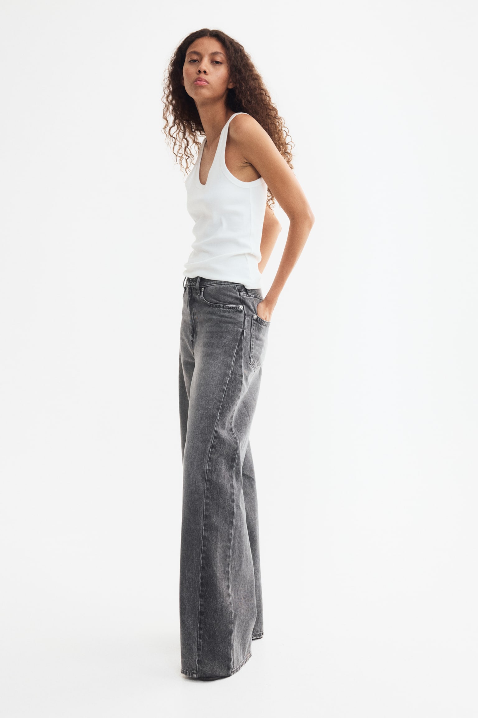 Un paio di jeans a 5 tasche è mostrato in vista frontale, realizzato in denim grigio scuro lavato con scoloriture visibili sulle cosce. Presentano una vita regolare con chiusura a zip e bottone, e una gamba dritta che è ampia dalla coscia all'orlo, raggiungendo una lunghezza regolare sulla parte superiore del piede. - 1