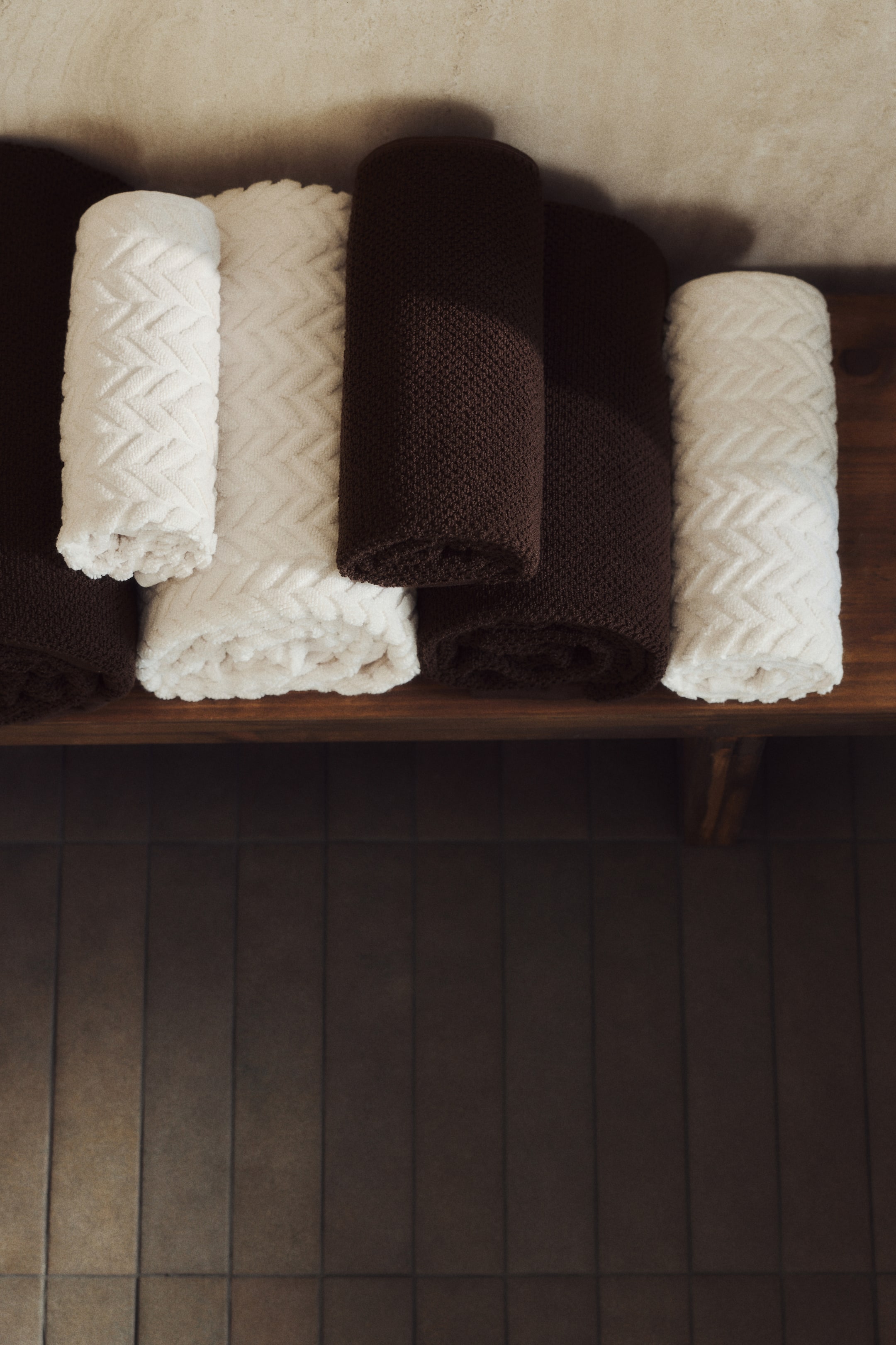 Agrandir l'image: Les serviettes roulées sont disposées horizontalement, montrant des couleurs alternées de blanc et de brun foncé. Les serviettes blanches présentent un motif texturé en chevrons, tandis que les serviettes brun foncé affichent un tissage subtilement texturé.