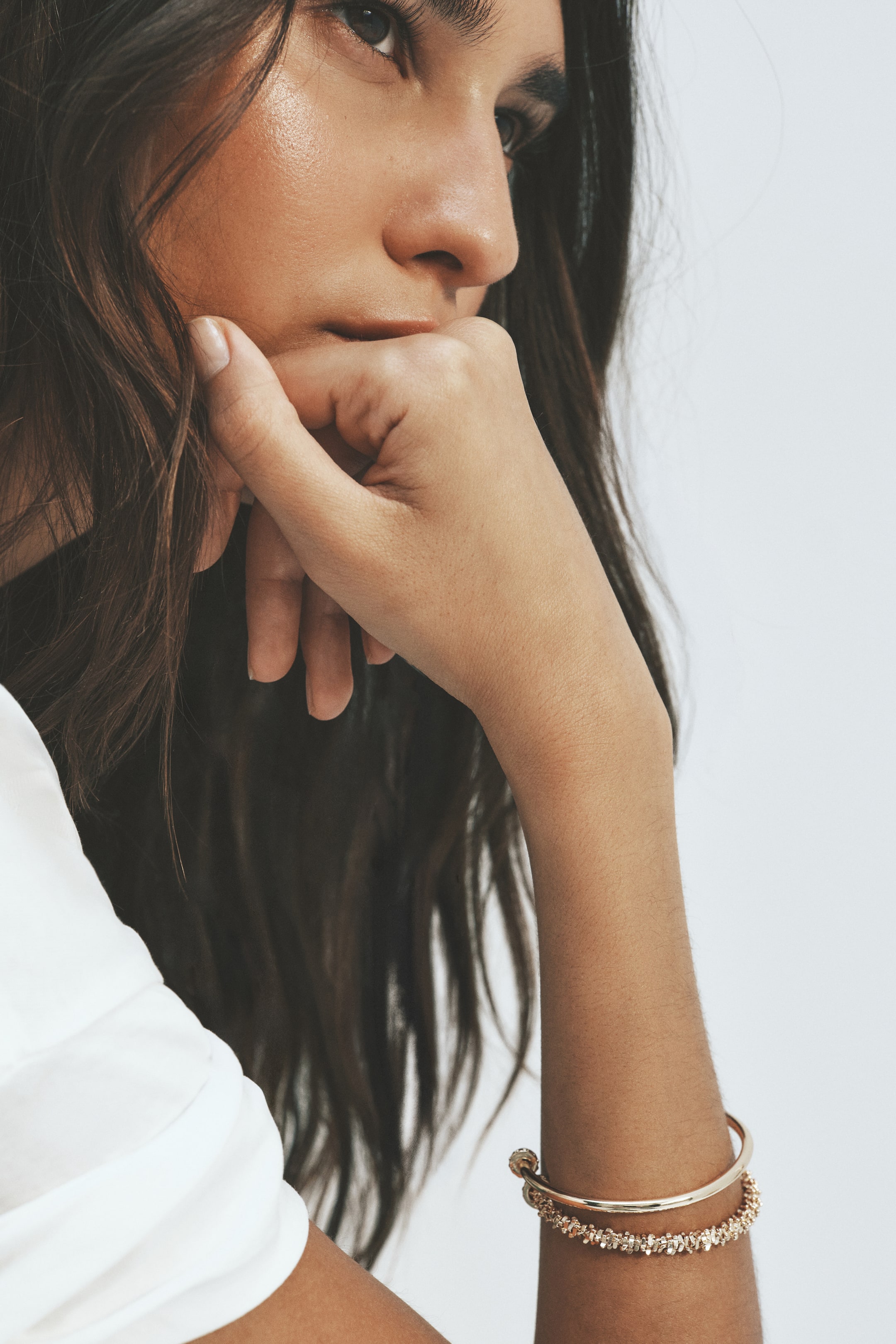 View larger image: Two gold-toned bracelets are worn on a wrist, shown from a slight angle. The upper bracelet is a smooth, thin bangle with a knot detail, and the lower bracelet is a wider, textured cuff adorned with sparkling elements.
