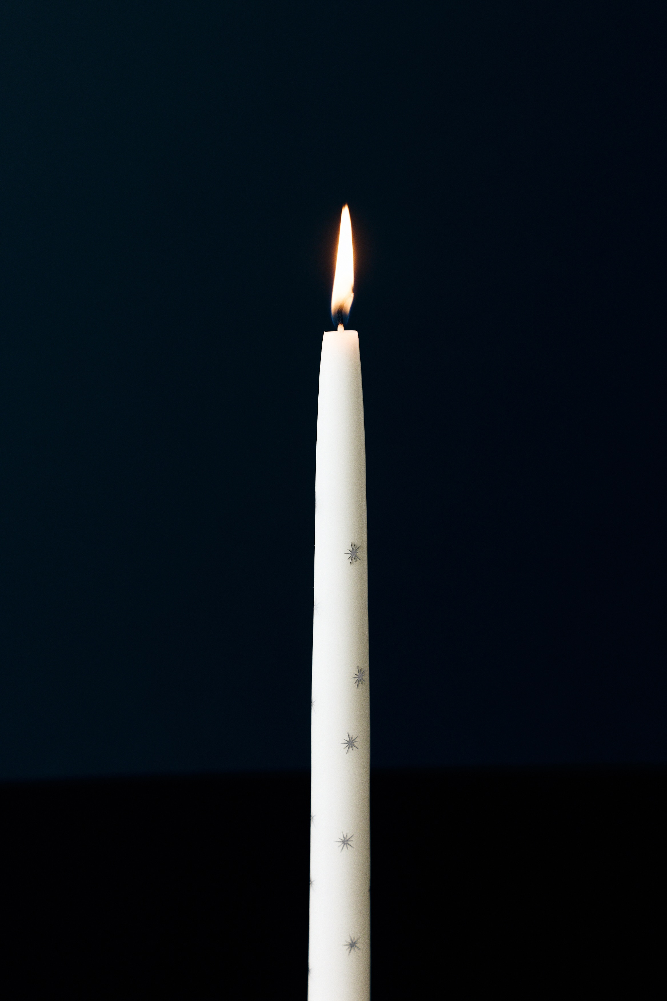 Een paar crÃ¨mekleurige dinerkaarsen staat rechtop naast elkaar, met een verspreid patroon van kleine zilveren stervormige uitbarstingen. De kaarsen lopen geleidelijk taps toe naar de top, met korte lonten die uit de toppen steken.