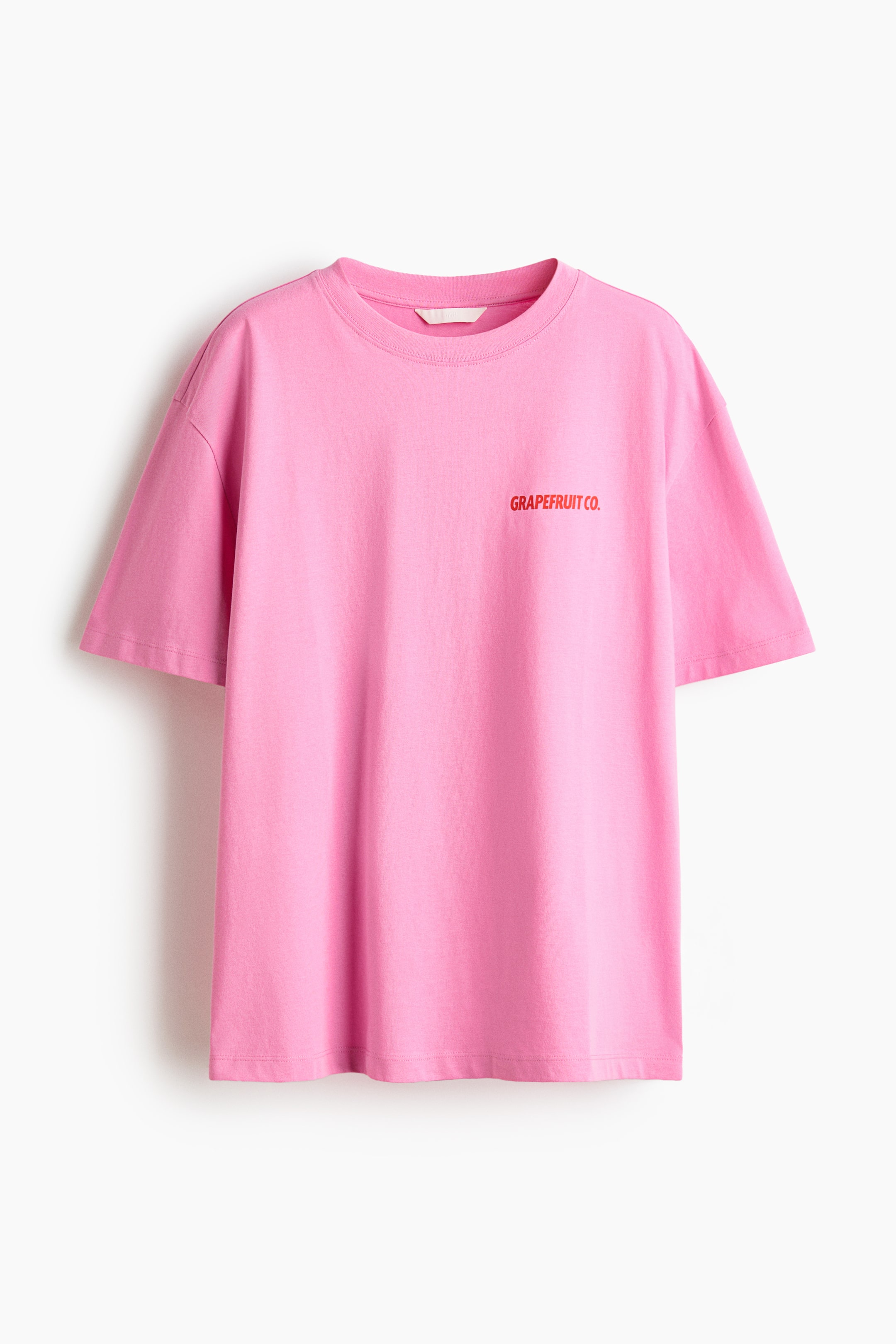 View larger image: An oversized T-shirt in pink cotton jersey is showcased from the front, featuring a round neckline, subtly dropped shoulders, and short sleeves. Red text reading "GRAPEFRUIT CO." appears on the left chest area.