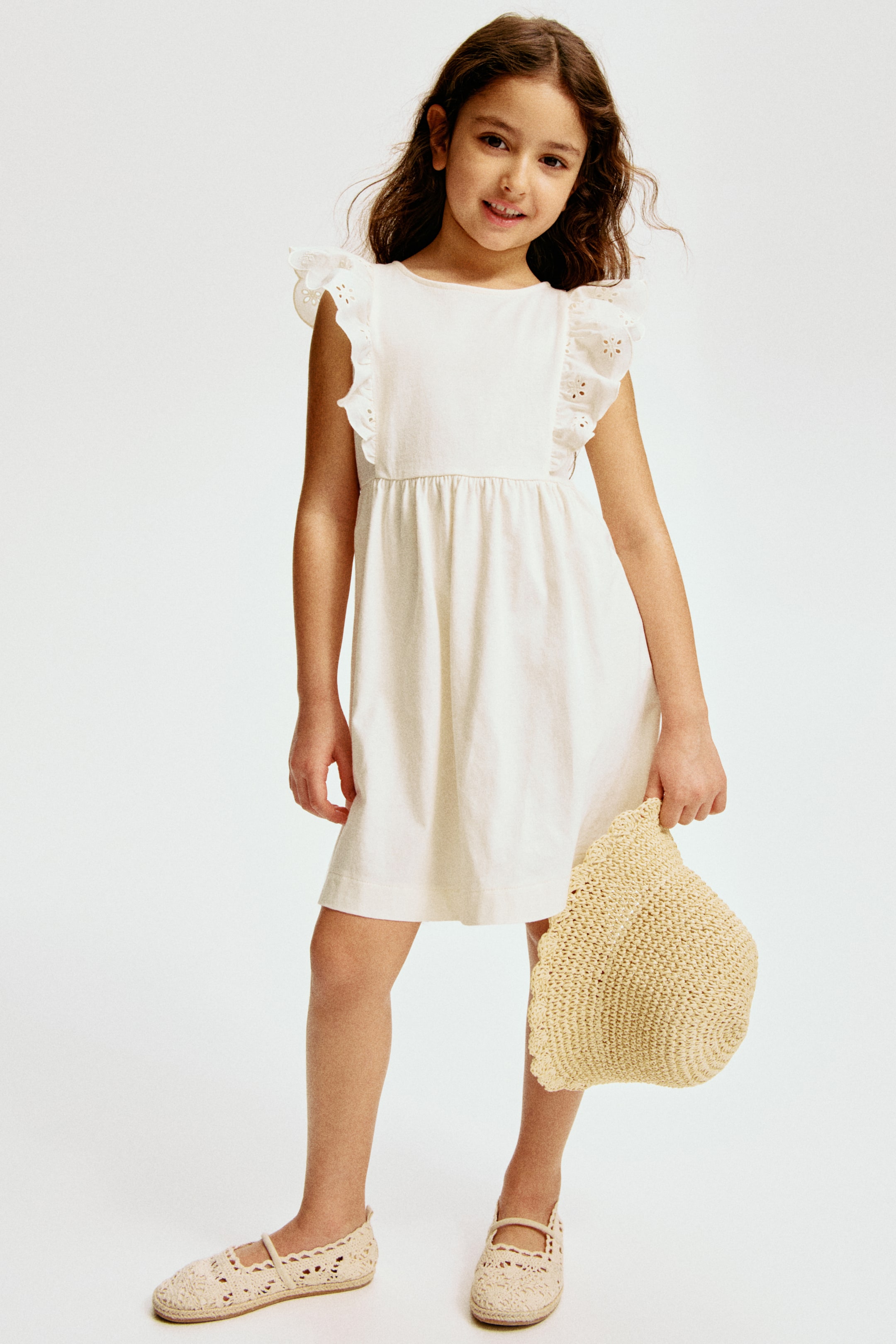 View larger image: This off-white frock showcases a round neckline complemented by ruffled, eyelet-embroidered shoulder accents. Crafted with an empire waist, it transitions into a gathered, flowing skirt that gracefully falls just above the knee.
