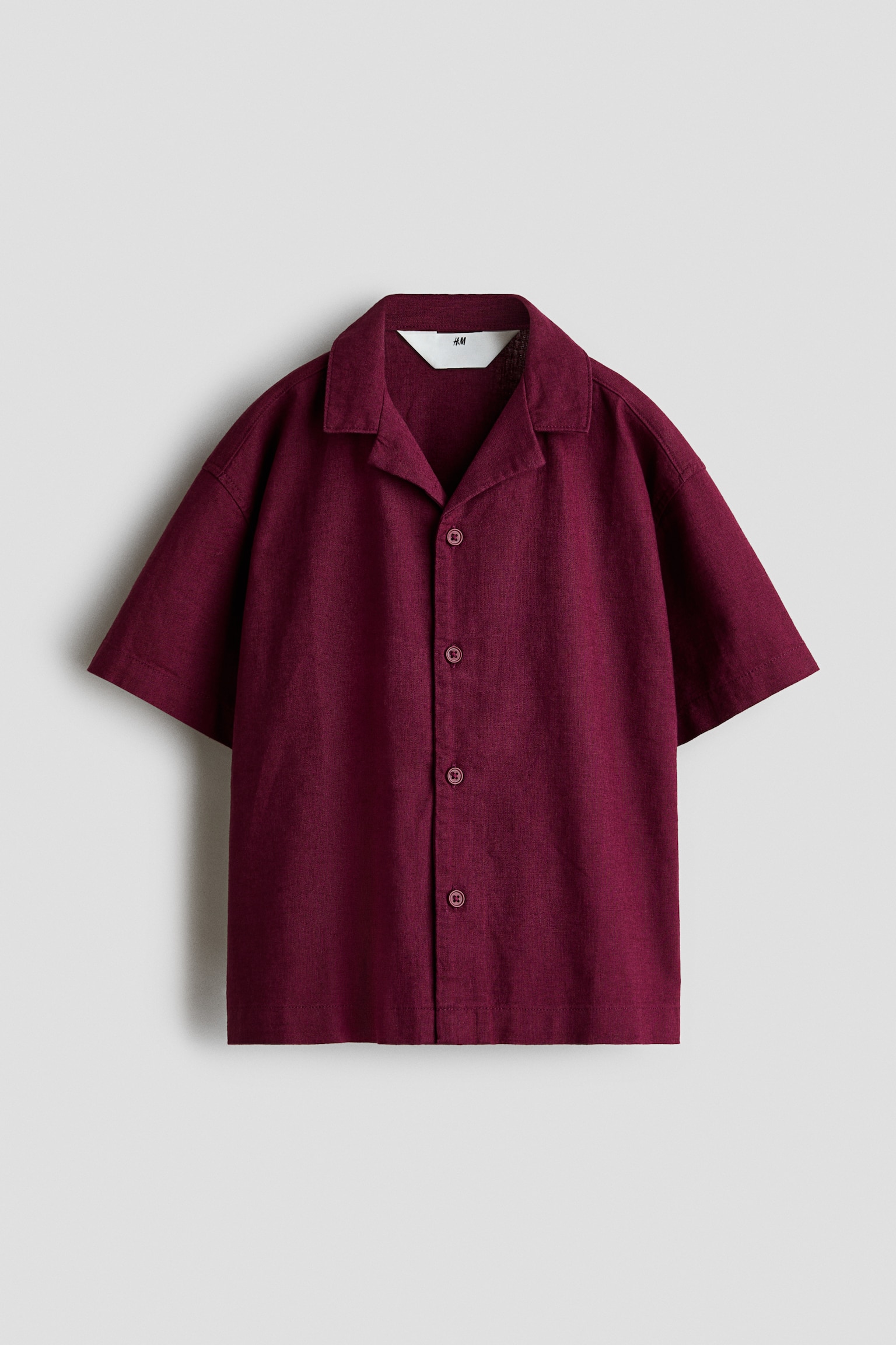 Má»t chiếc áo sÆ¡ mi tay ngắn bằng chất liá»u pha linen-cotton mà u burgundy có bá» mặt dá»t ná»i ÄÆ°á»£c chụp từ phÃa trưá»c, vá»i cá» resort và phần nẹp cà i nút phÃa trưá»c gá»m bá»n nút cùng tông. Ão có phom dáng thoải mái vá»i vai xuôi nhẹ và lai áo thẳng.