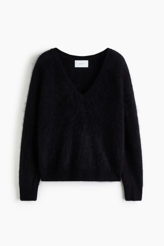 Un pull en laine noire, doux et duveteux, est présenté de face, avec un col en V côtelé, des épaules tombantes et des manches longues. Il met en valeur une finition douce et texturée, avec des bords-côtes aux poignets et à lâourlet. - 1