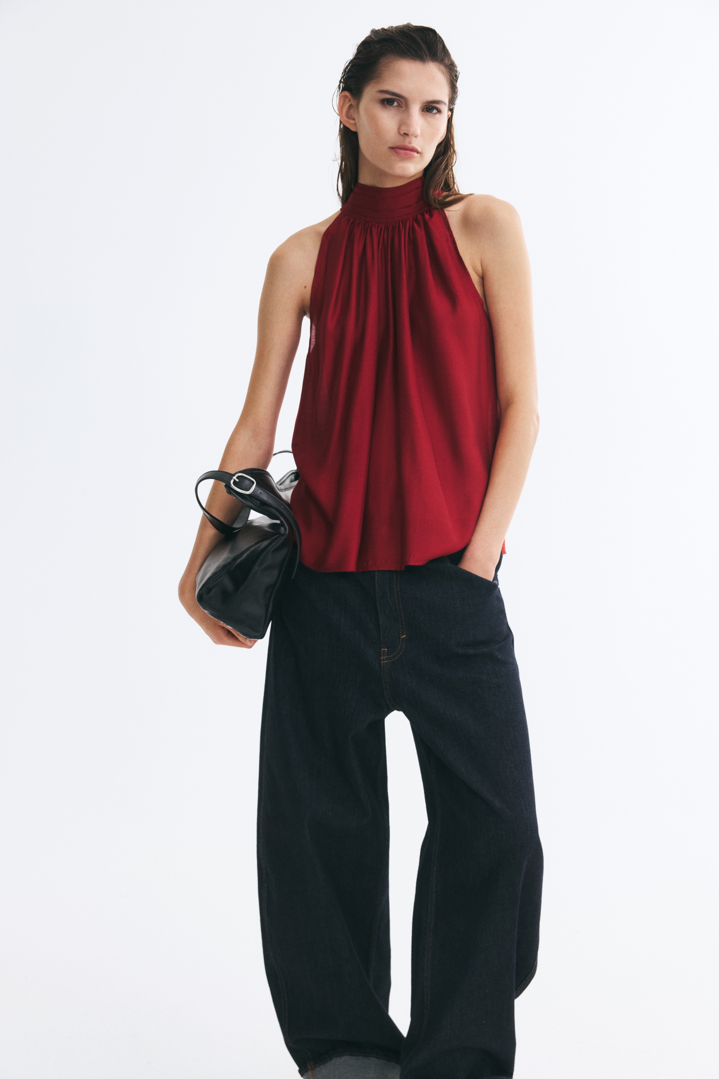 A sleeveless A-line top in a deep red weave with a subtle sheen is hanging front-facing. The design features a pleated stand collar with gathered fabric draping down to a straight-cut hem.