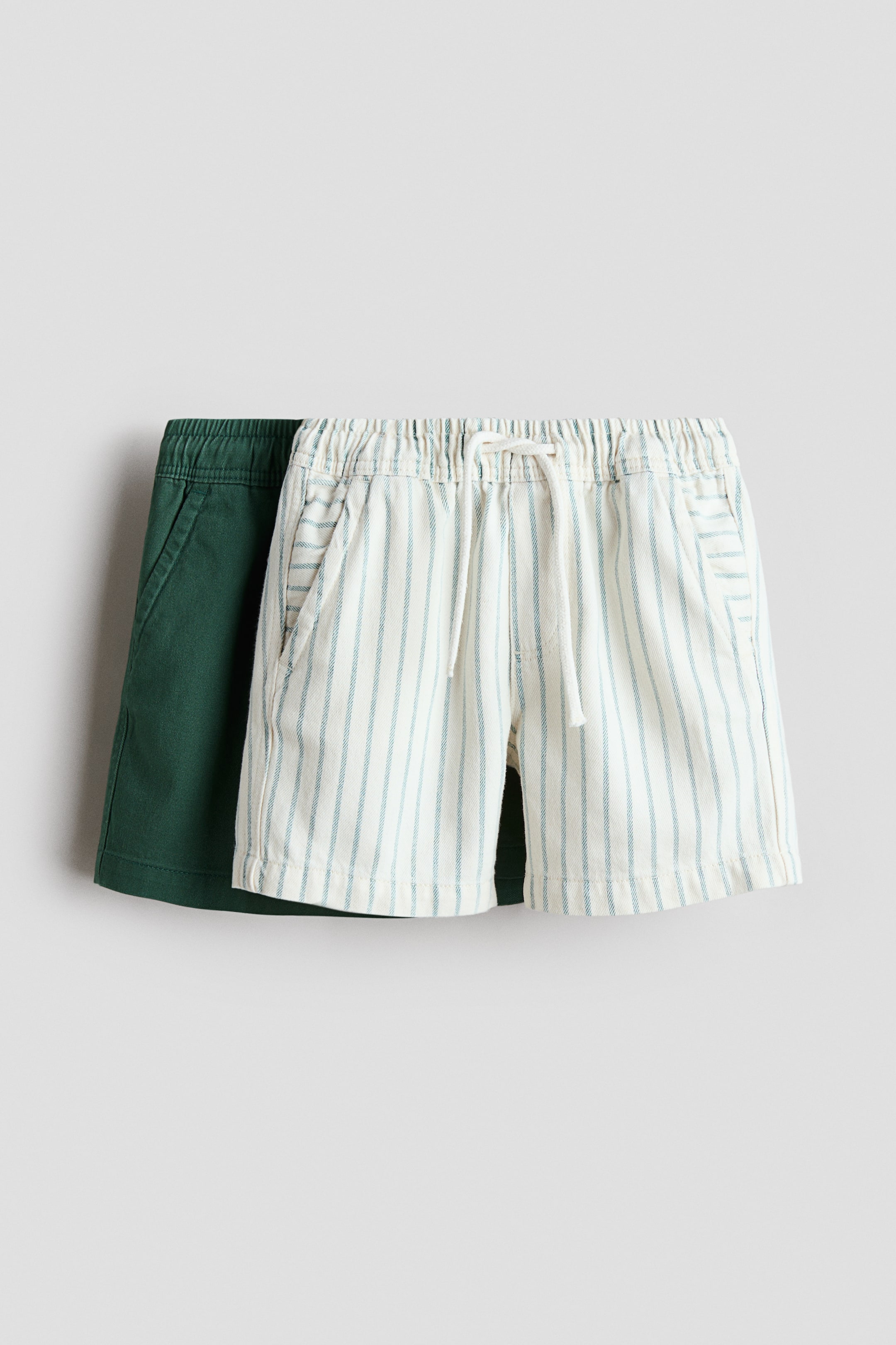 View larger image: Two pairs of shorts are being showcased, with an off-white, blue striped pair layered in front of a dark green pair. The front pair features an elasticated waistband with a white drawstring and front pockets, while the green pair also displays an elasticated waistband and front pockets.