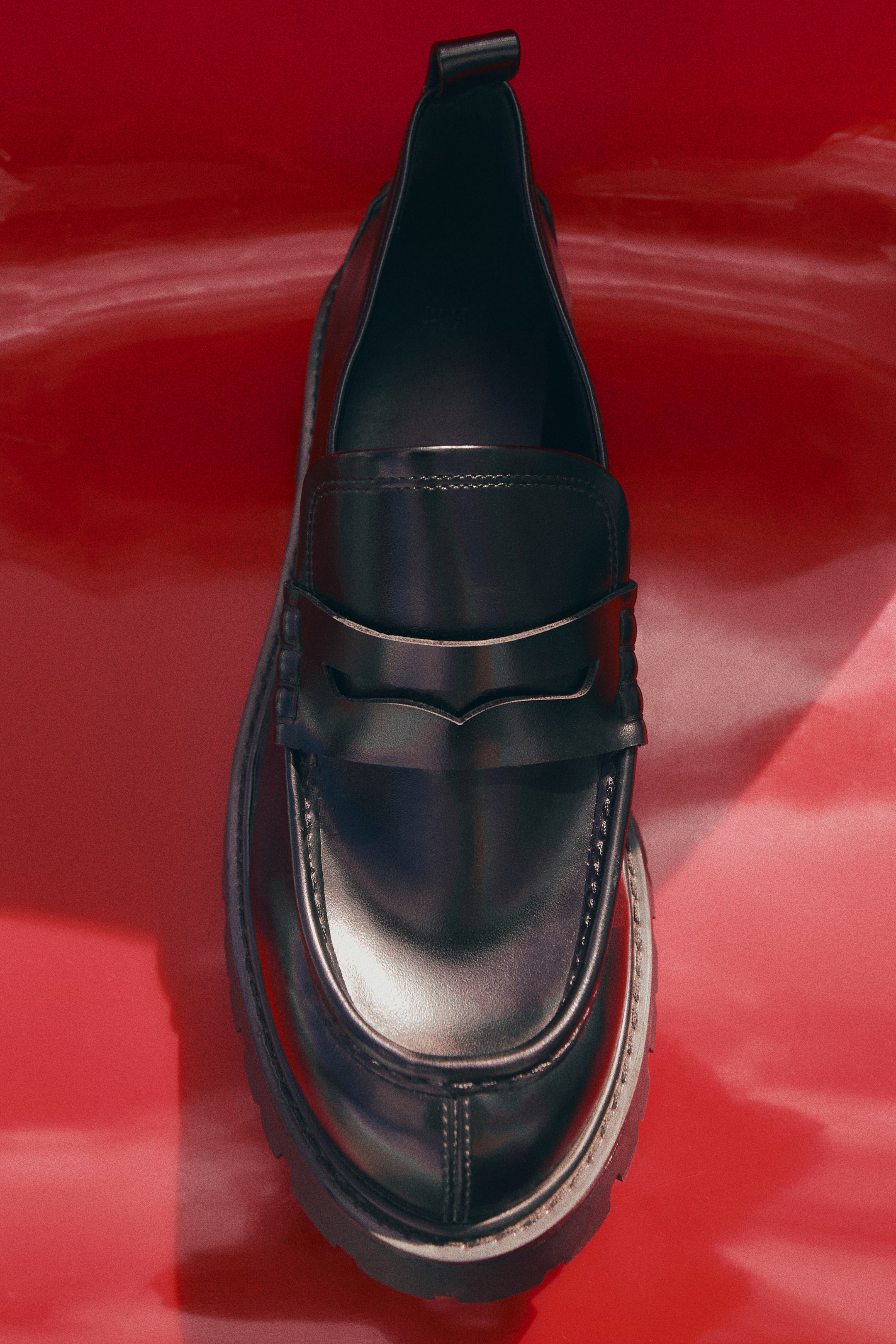 Größeres Bild ansehen: Ein einzelner schwarzer Loafer ist frontal ausgerichtet und präsentiert ein glattes Obermaterial mit Mokassin-Naht und einem klassischen Pennyloafer-Riegel. Der Schuh verfügt über eine Zugschlaufe an der Ferse und ist auf einer robusten, profilierten Sohle gesetzt.