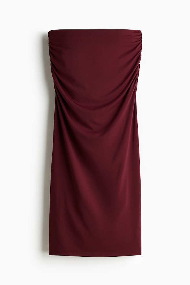 Un vestido mini sin tirantes color granate se muestra desde el frente. Presenta un fruncido prominente a lo largo de ambas costuras laterales en el busto, que luego se reúne hacia el centro, creando suaves pliegues en la parte delantera del vestido. - 1