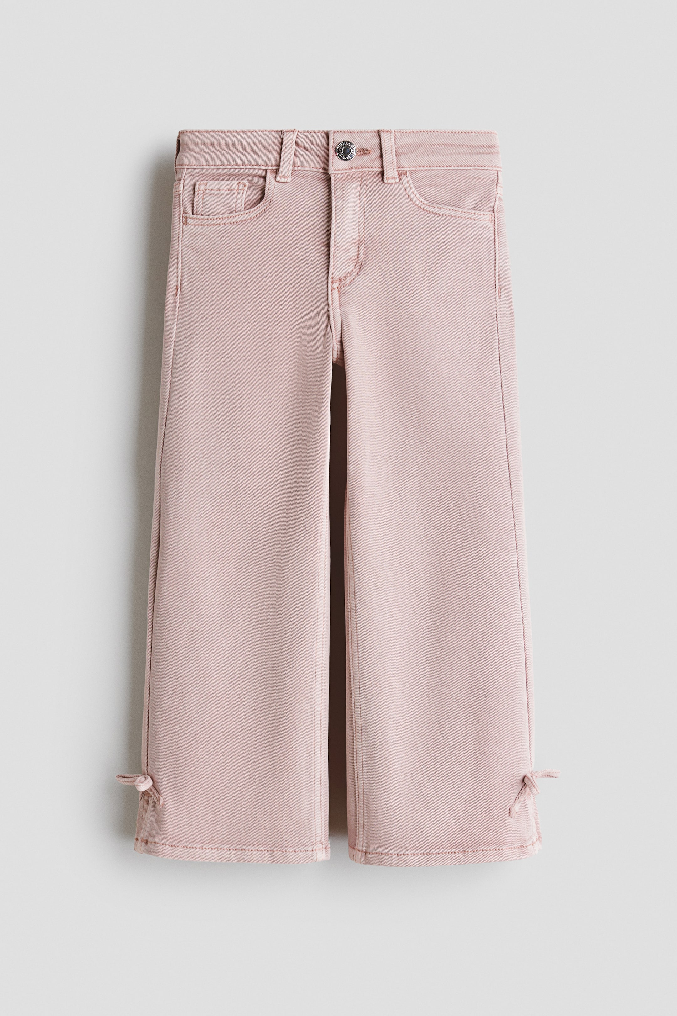 Visualizza immagine più grande: Jeans in denim rosa distesi, caratterizzati da una vestibilità aderente su fianchi e cosce e gambe larghe. Sono progettati con chiusura a bottone e zip, tasche frontali e piccoli lacci decorativi all'orlo esterno di ogni gamba.