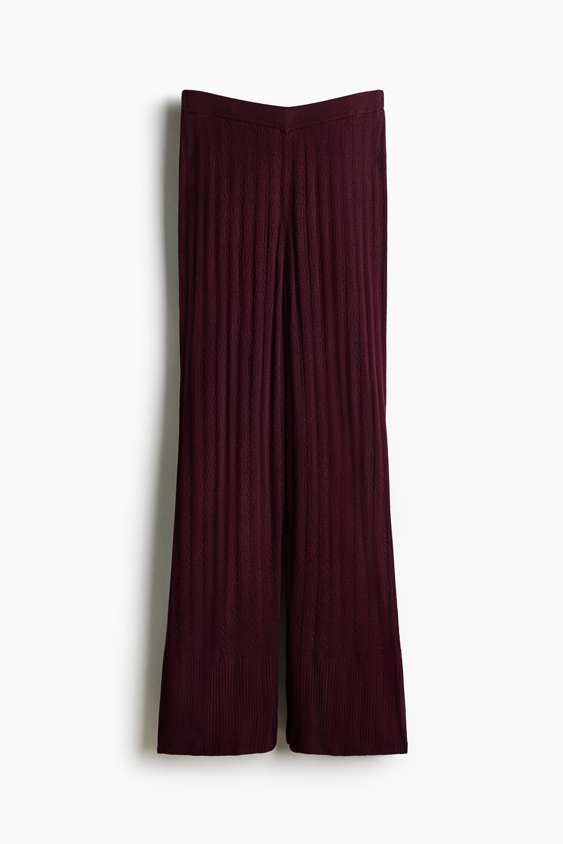 View larger image: The deep-red knitted pants display a vertical cable-knit pattern along the legs. A ribbed waistband and wide ribbed hems are shown, with the front of the waistband featuring a V-shape.
