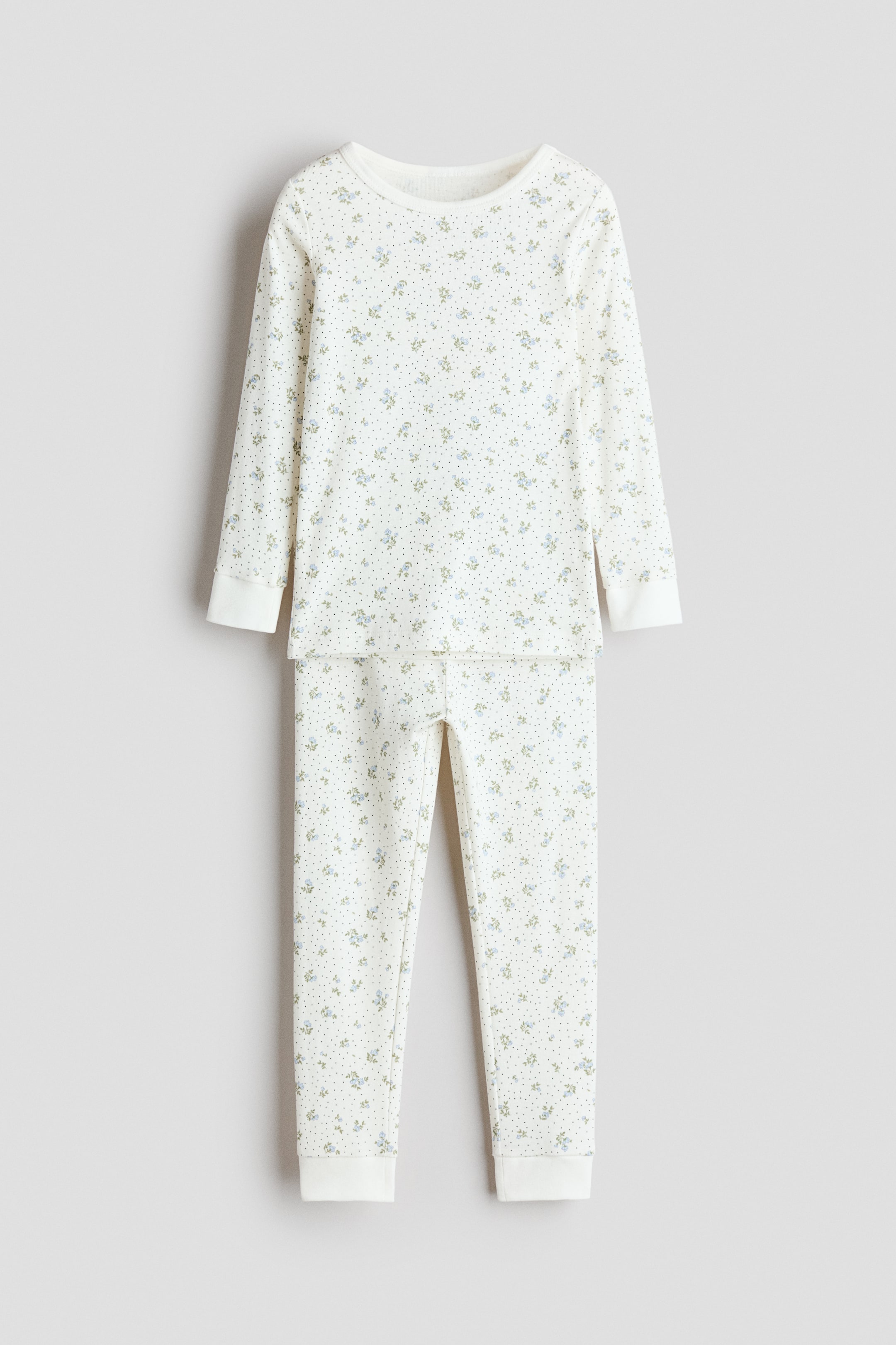 View larger image: A two-piece pajama set is laid out flat, front-facing, showcasing an off-white base adorned with a scattered pattern of small blue floral clusters and tiny gray dots. The long-sleeved top features a round neckline and ribbed cuffs, while the matching long pants complete the set with ribbed cuffs at the ankles.