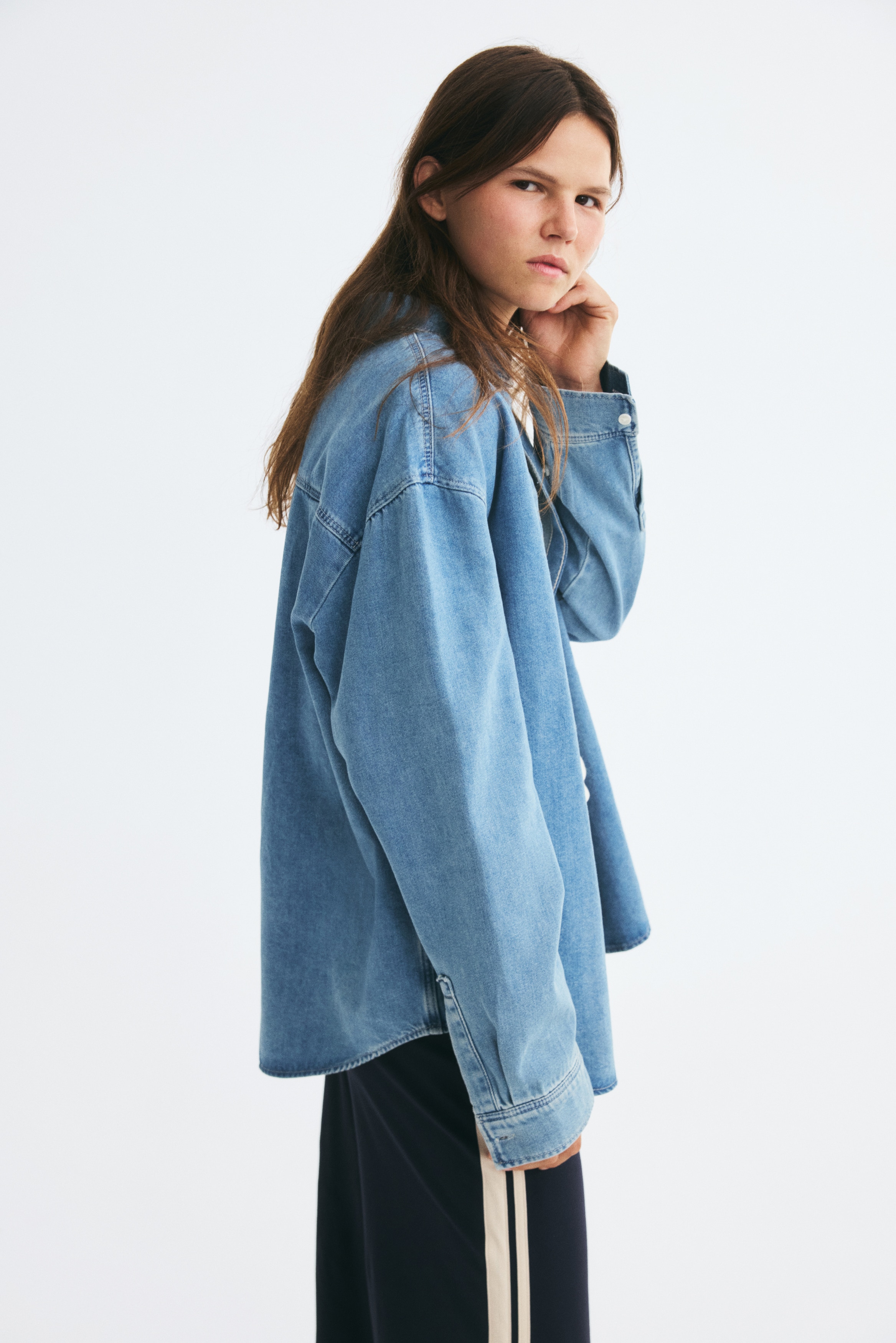 Viene presentata una vista anteriore di una camicia oversize in denim blu super morbido e leggero come una piuma, caratterizzata da un colletto, un'abbottonatura anteriore, spalle scese, maniche lunghe con abbottonature e polsini con bottoni, un carré posteriore e un orlo arrotondato.