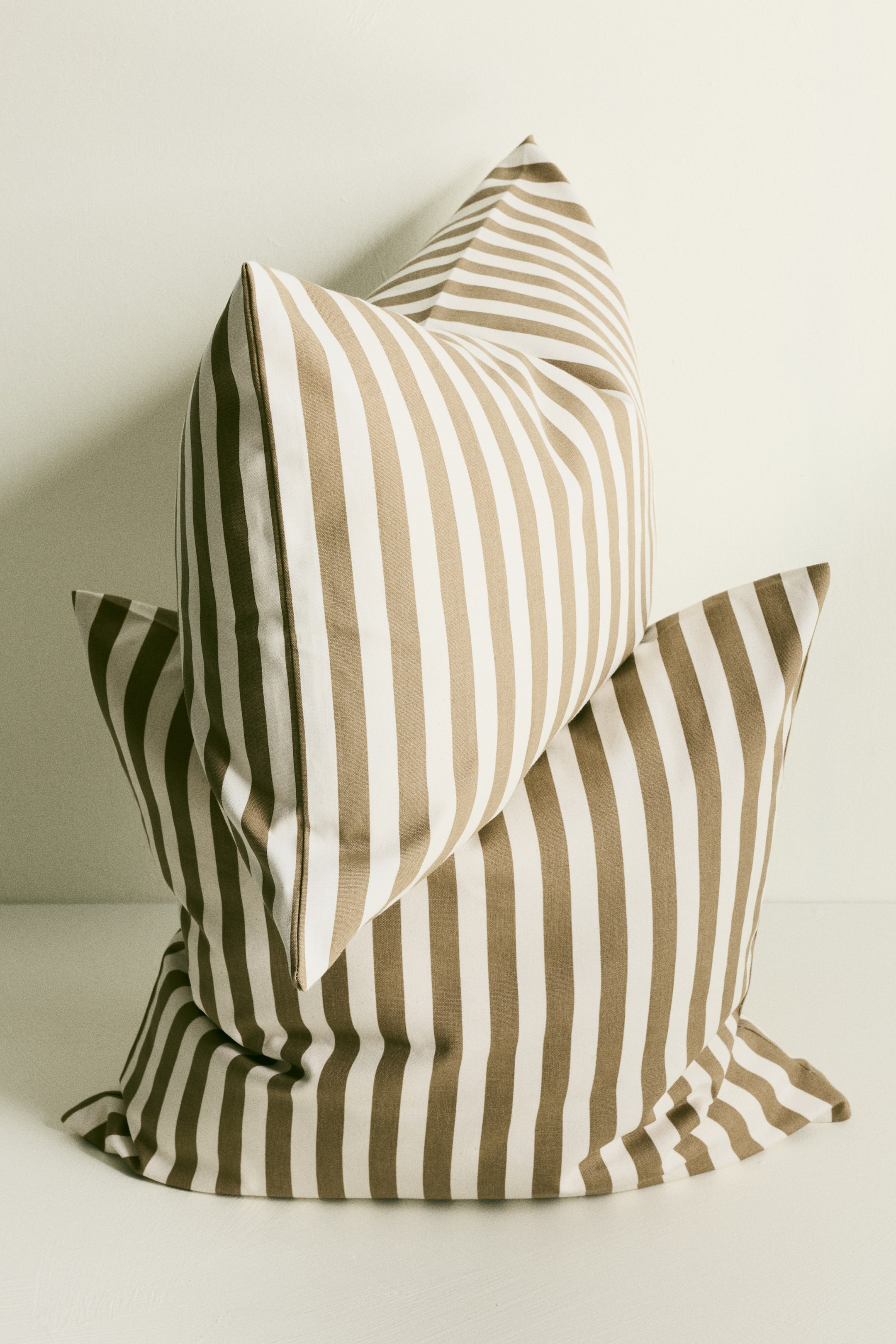 View larger image: Two rectangular cushion covers are stacked, with the top cover angled to show its front and side. Both covers feature vertical stripes in alternating beige and cream colors, appearing to be made of a textured canvas fabric.