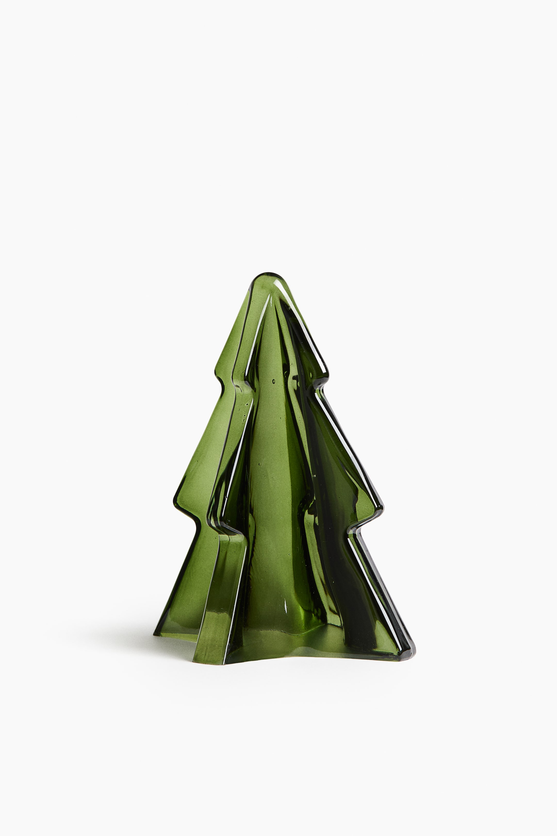 Ampliar la imagen: Una pequeña decoración navideña de vidrio con forma de árbol de abeto está colocada en posición vertical, mostrando su color verde translúcido y su estructura tridimensional con paneles verticales que se intersectan. El árbol estilizado presenta bordes suaves y redondeados, y se estrecha hacia la parte superior, creando una silueta minimalista.