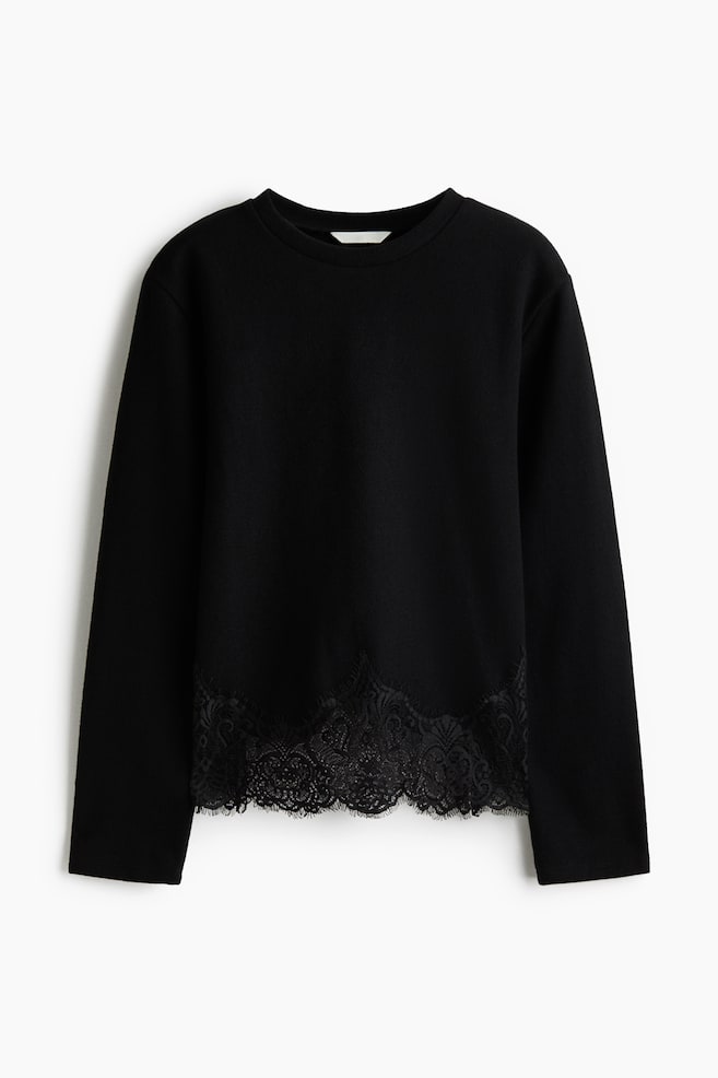 A black, loose-fit jersey top is shown from the front, featuring a round, rib-trimmed neckline and long, straight sleeves. The design features a scalloped black eyelash lace trim along the bottom hem. - 1