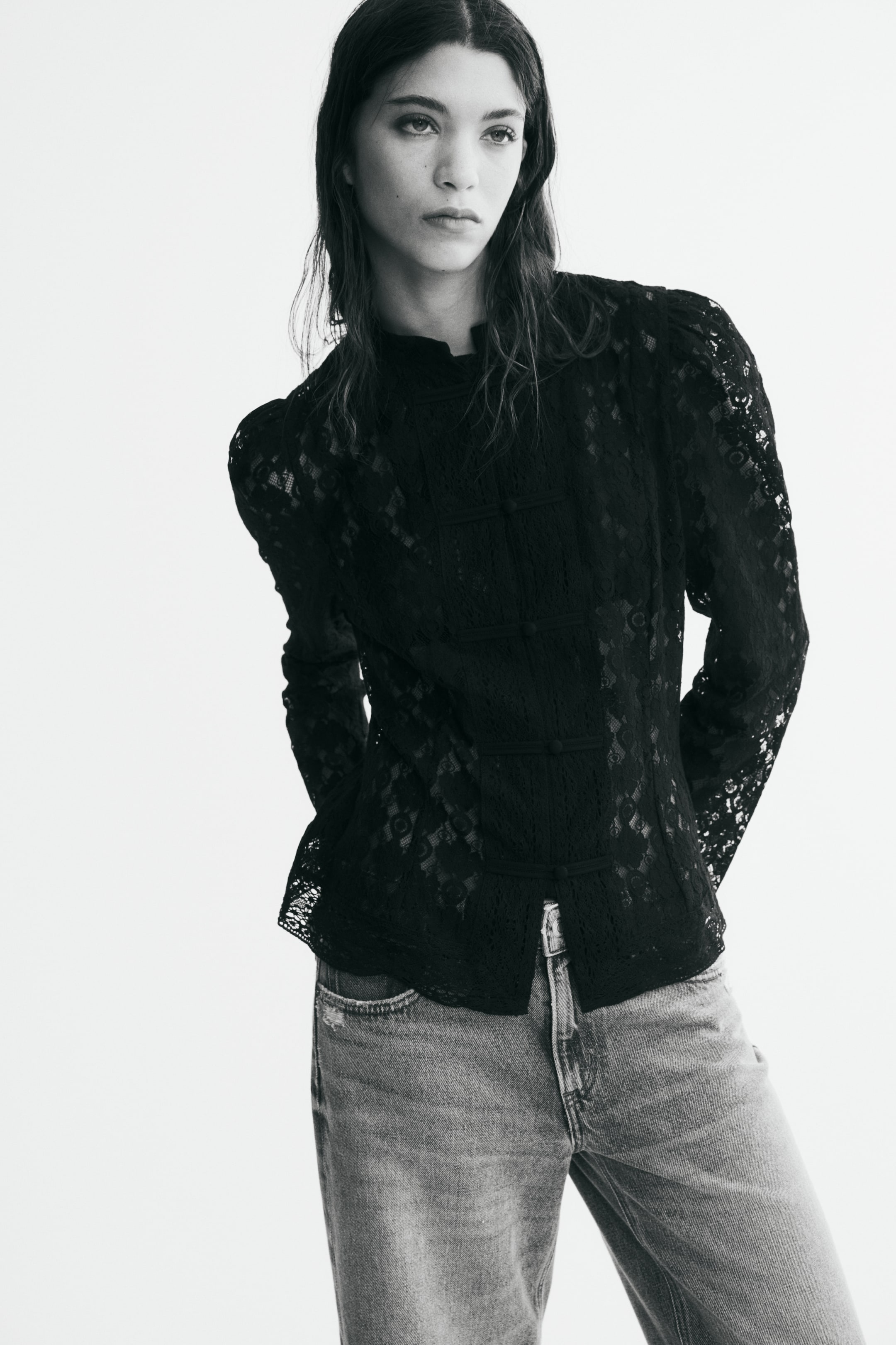 Ver imagen más grande: La modelo lleva una blusa negra de encaje transparente con cuello mao, botones delanteros anudados y mangas largas abullonadas. La blusa se combina con unos vaqueros de denim.