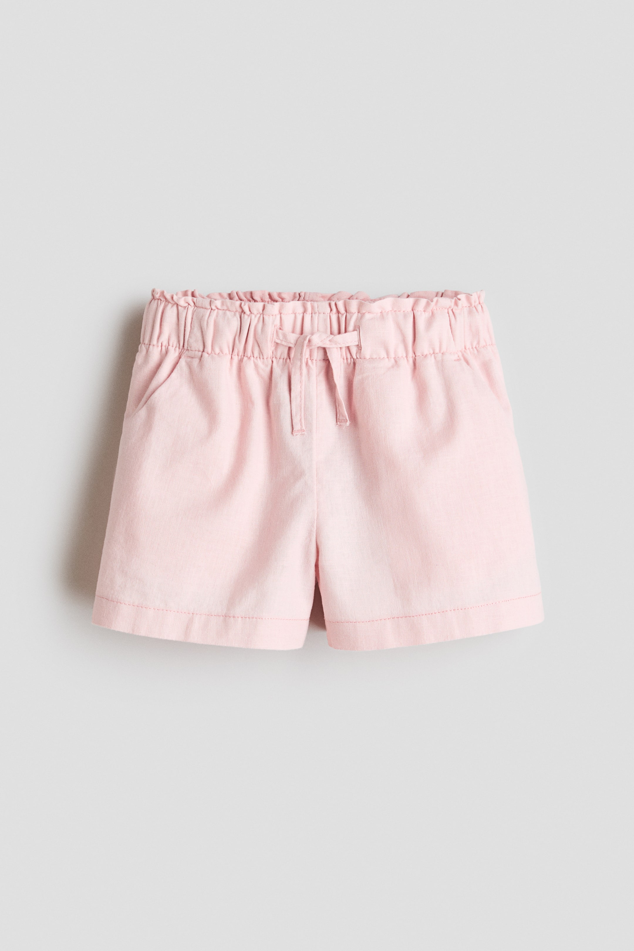 View larger image: Loose-fit pink shorts are showcased from the front view. They boast an elasticated pull-on waistband, complete with a slender drawstring tied at the center, and diagonal side pockets.