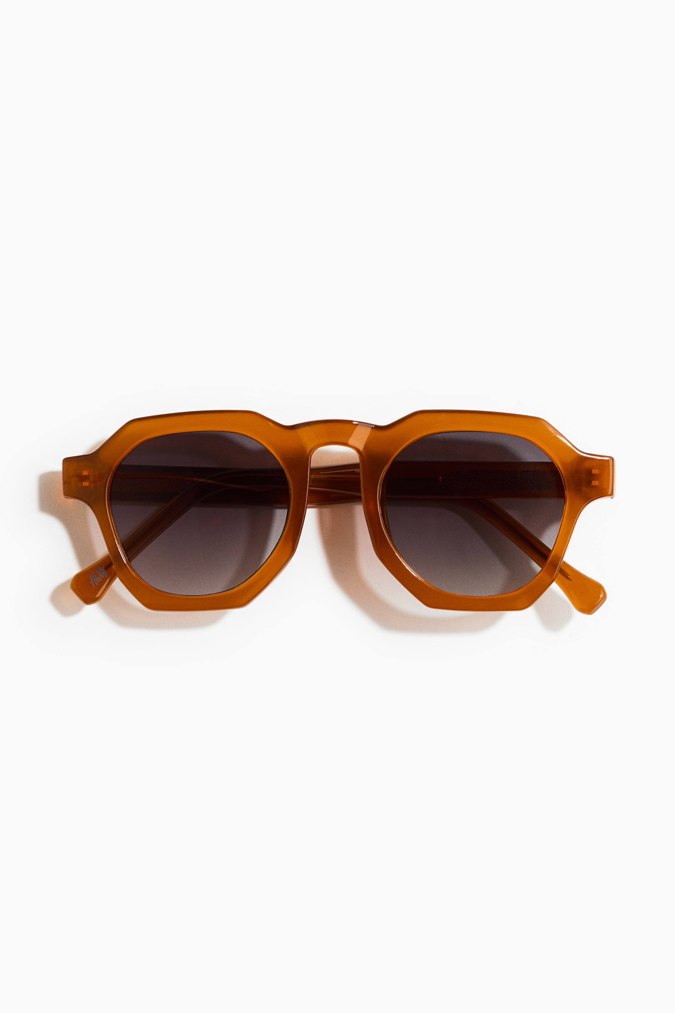 View larger image: Hexagon-shaped sunglasses are displayed front-facing, showcasing translucent amber plastic frames and dark, gradient tinted lenses.