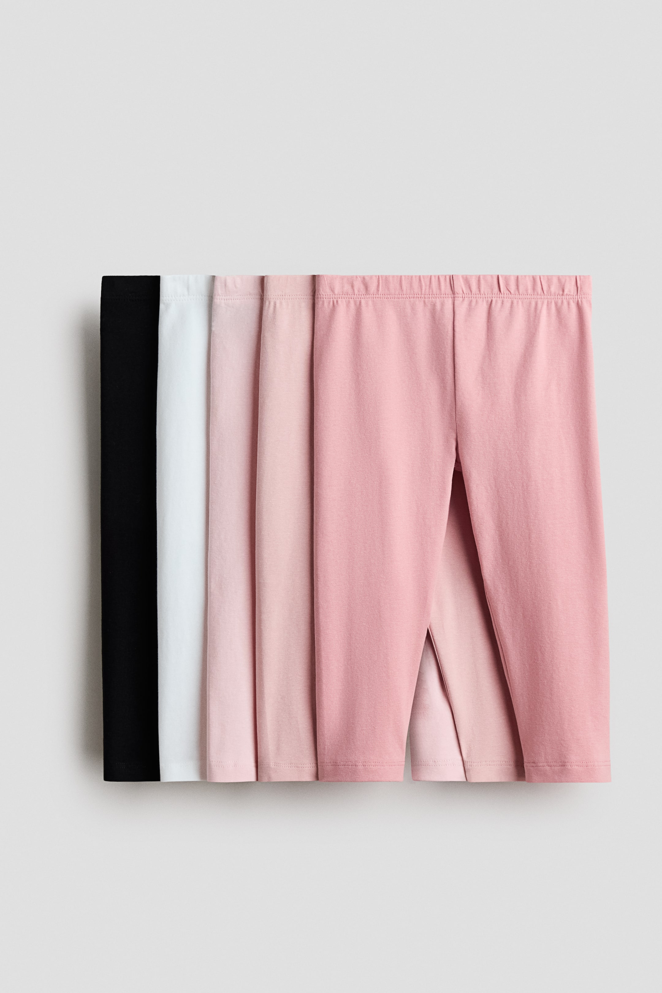 查看大圖: 五對3/4長的柔軟棉質針織緊身褲展示其正面。這些緊身褲的腰帶採用覆蓋式彈性設計,顏色包括黑色、白色和三種粉紅色調。