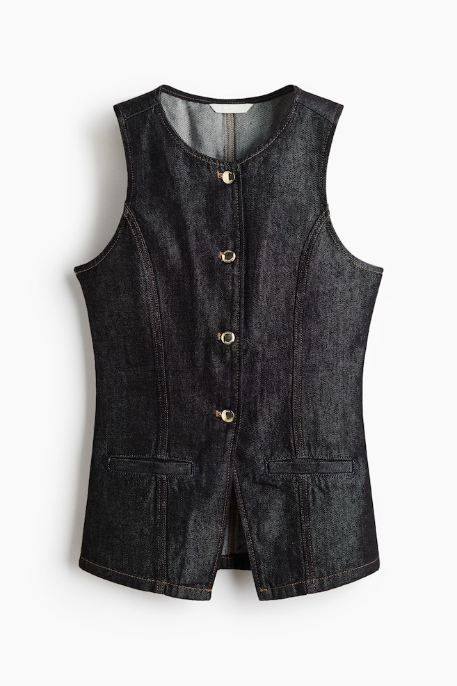 A dark, rigid denim waistcoat is being presented from the front, featuring a round neckline and four gold-toned metal buttons extending down its center. It is designed with front shaping seams and two fake welt pockets, and is gently flaring from the waist downwards, all accented by contrast stitching. - 1