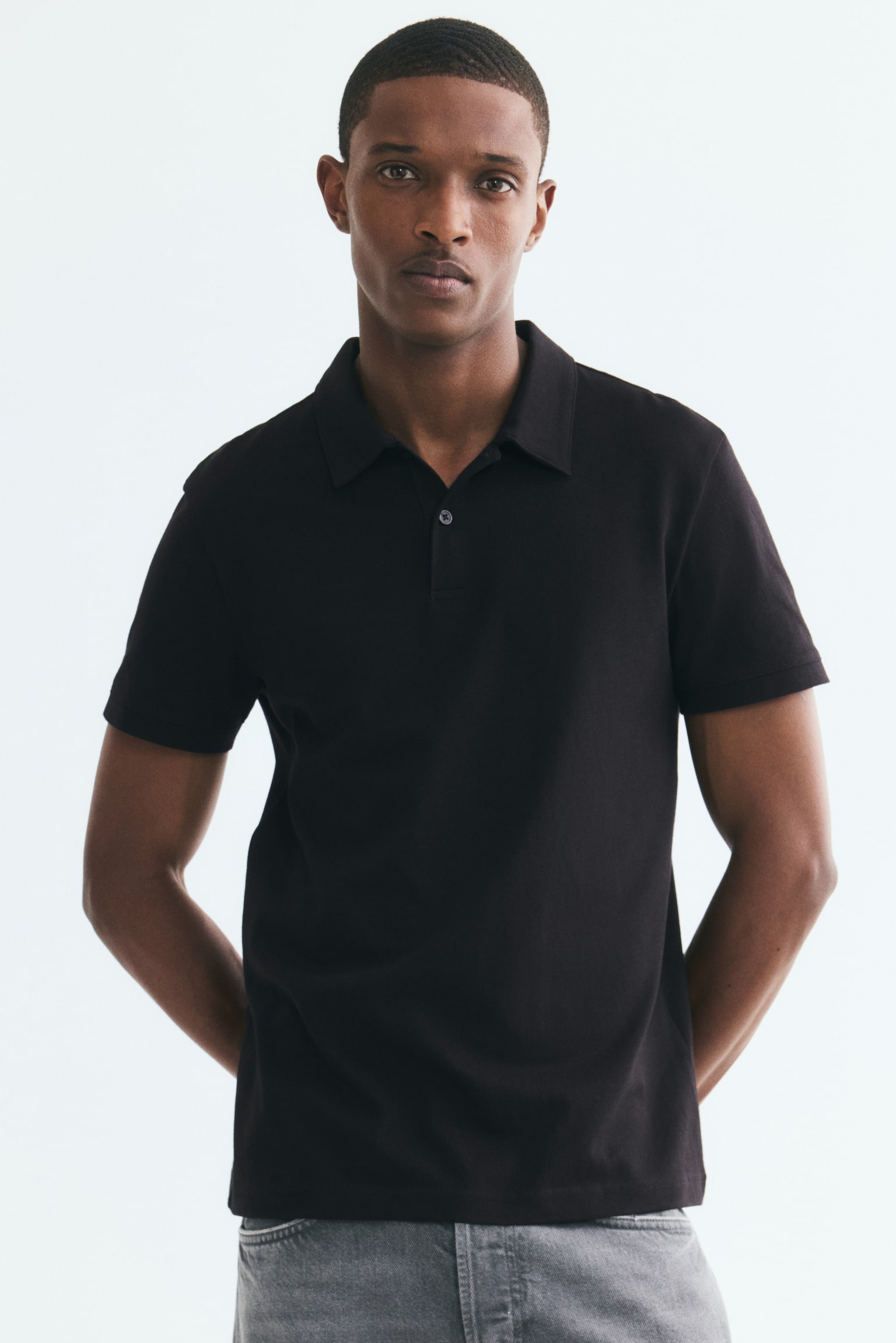 A black polo shirt shown from the front, featuring a pointed collar and a two-button placket with dark buttons, designed with short sleeves and a textured knit fabric. - 1